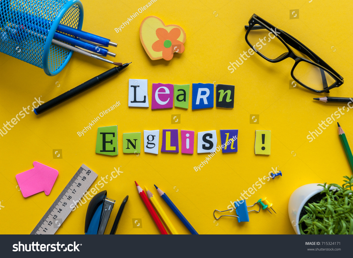 Word LEARN ENGLISH made with carved letters onyellow desk with office or school supplies, stationery. Concept of English language courses #715324171