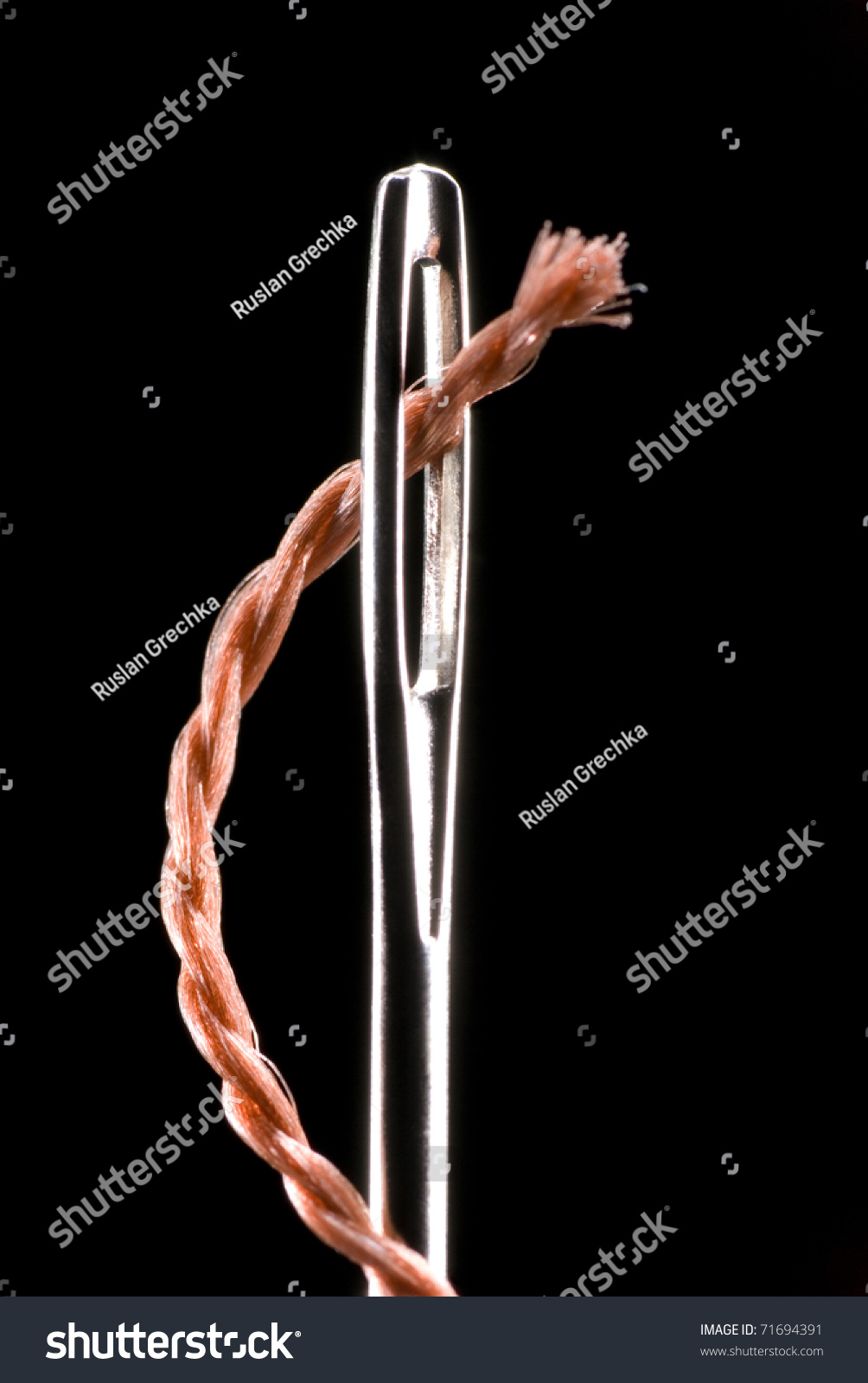 Metal needle and string. The string will penetrate into a metal aperture. A black background. #71694391