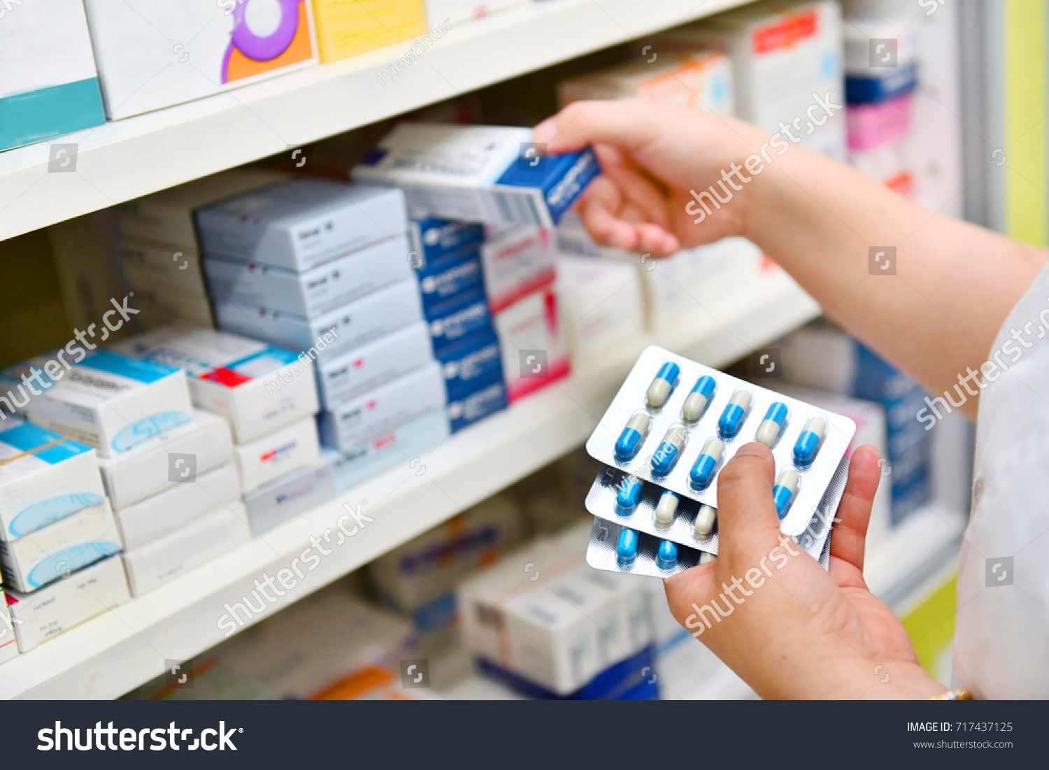 Pharmacist holding medicine box and capsule pack in pharmacy drugstore. #717437125