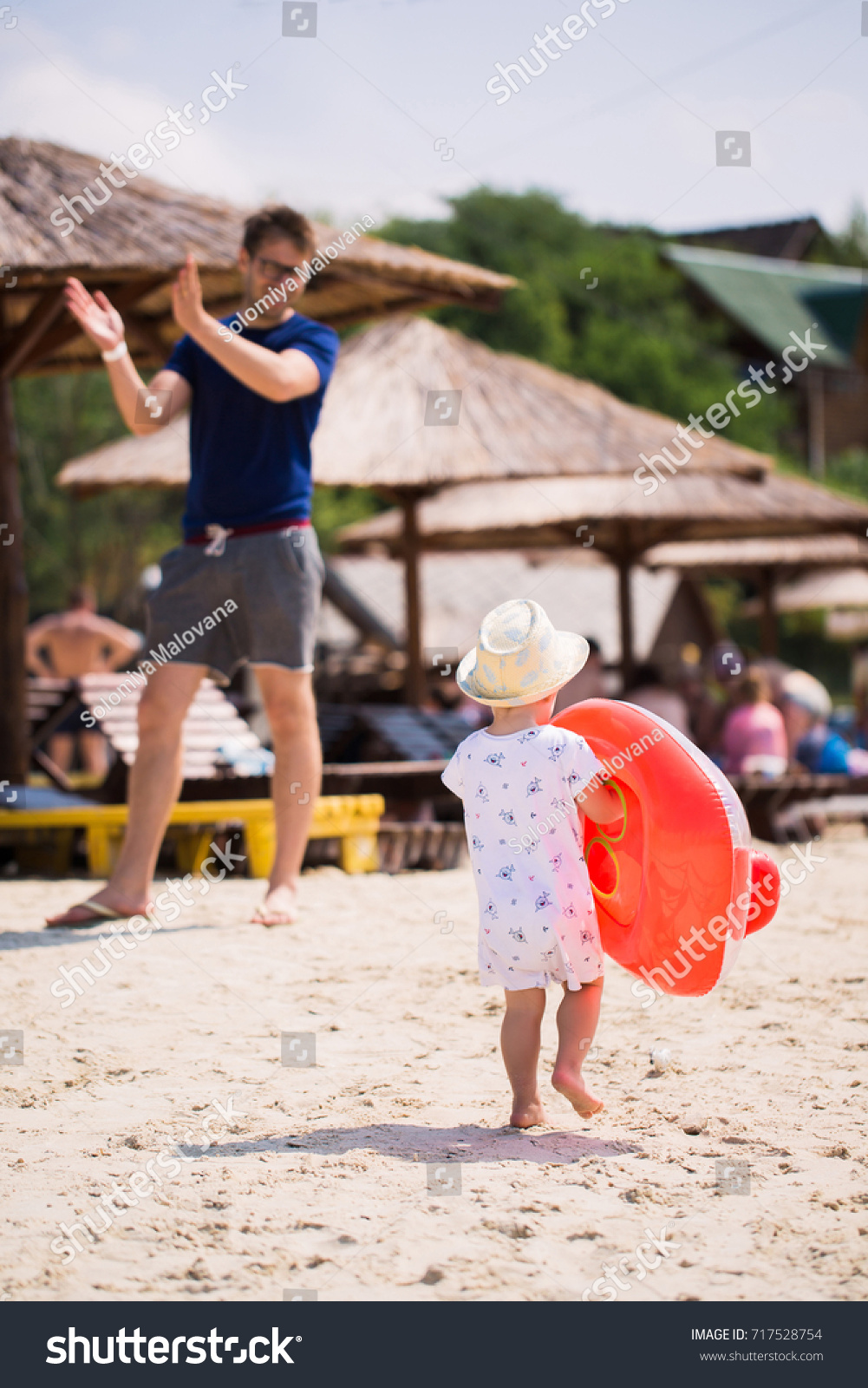 Back view of little boy who walking on the beach and keeping a float in hands #717528754