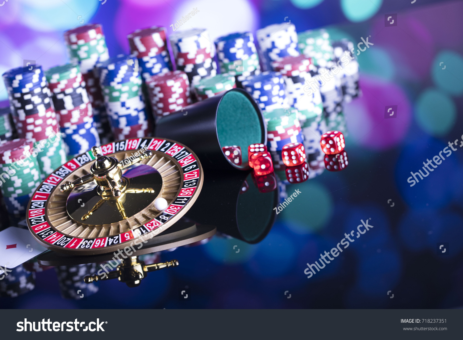 Casino theme. High contrast image of casino roulette, poker game, dice game, poker chips on a gaming table, all on colorful bokeh background.  #718237351