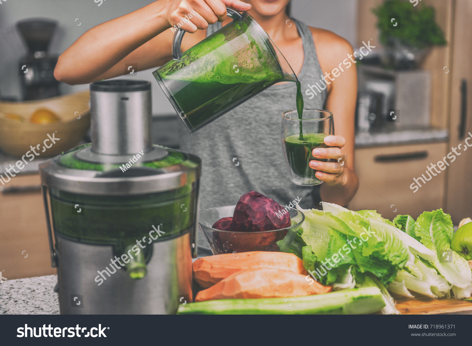 Woman juicing making green juice with juice machine in home kitchen. Healthy detox vegan diet with vegetable cold pressed extractor to extract nutrients for smoothie drink. #718961371