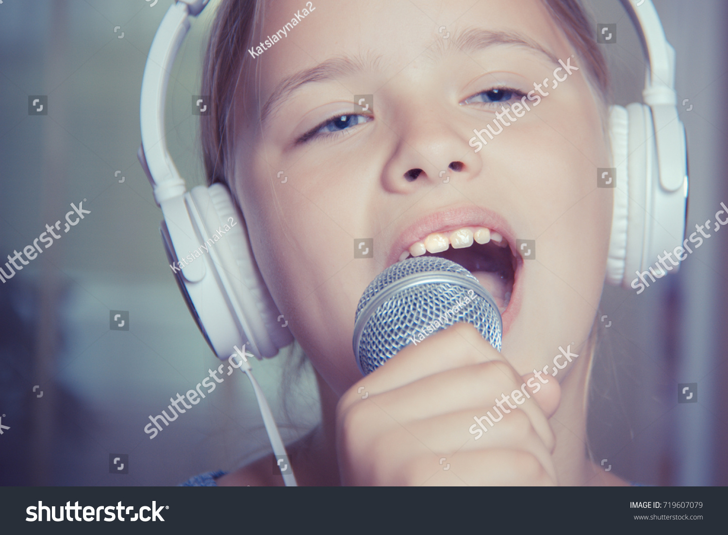 Closeup of singing caucasian child girl. Young girl emotionally sings into the microphone, holding it with hand #719607079