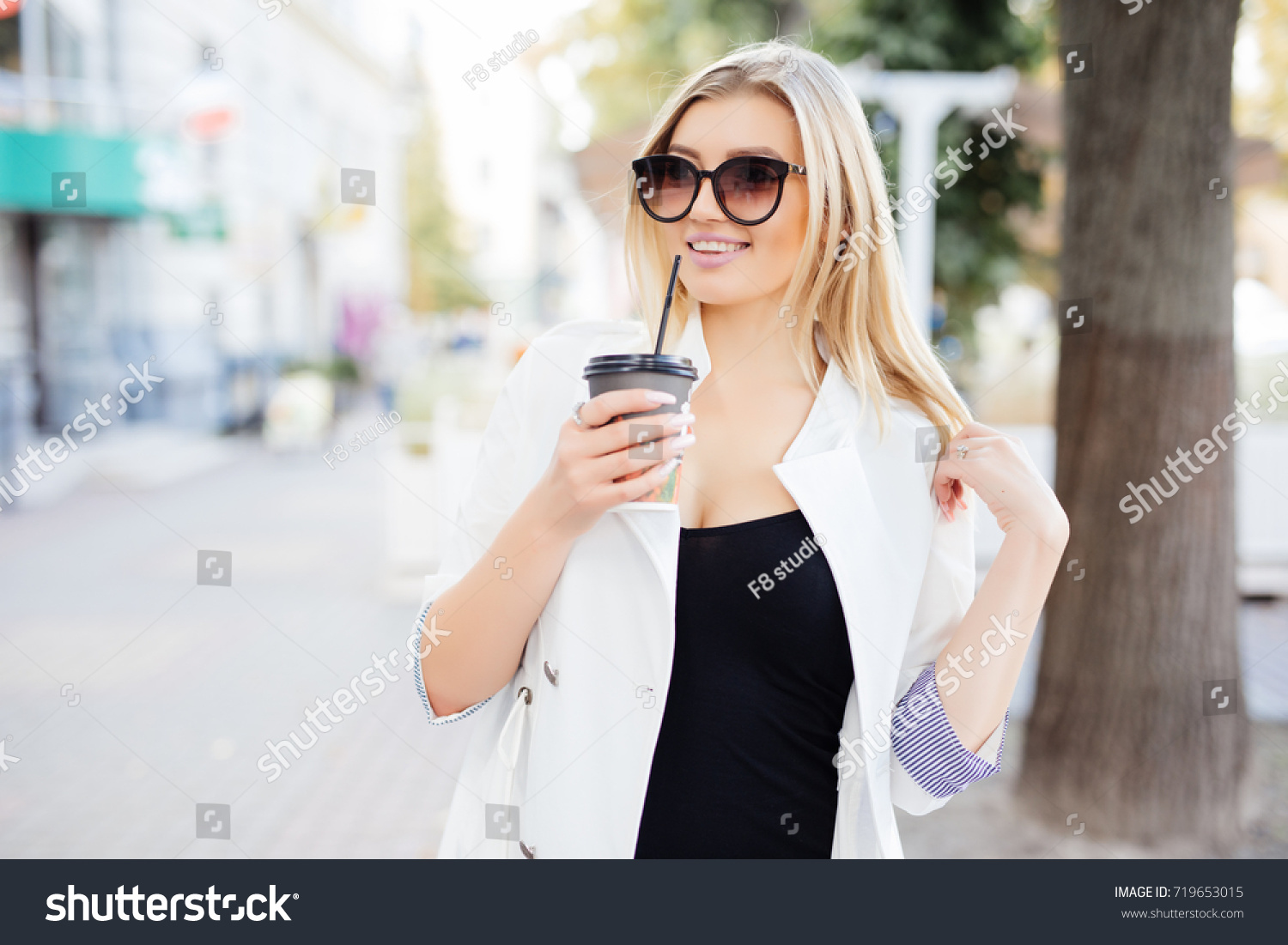 woman with take away cup of coffee or tea walking along the street. #719653015