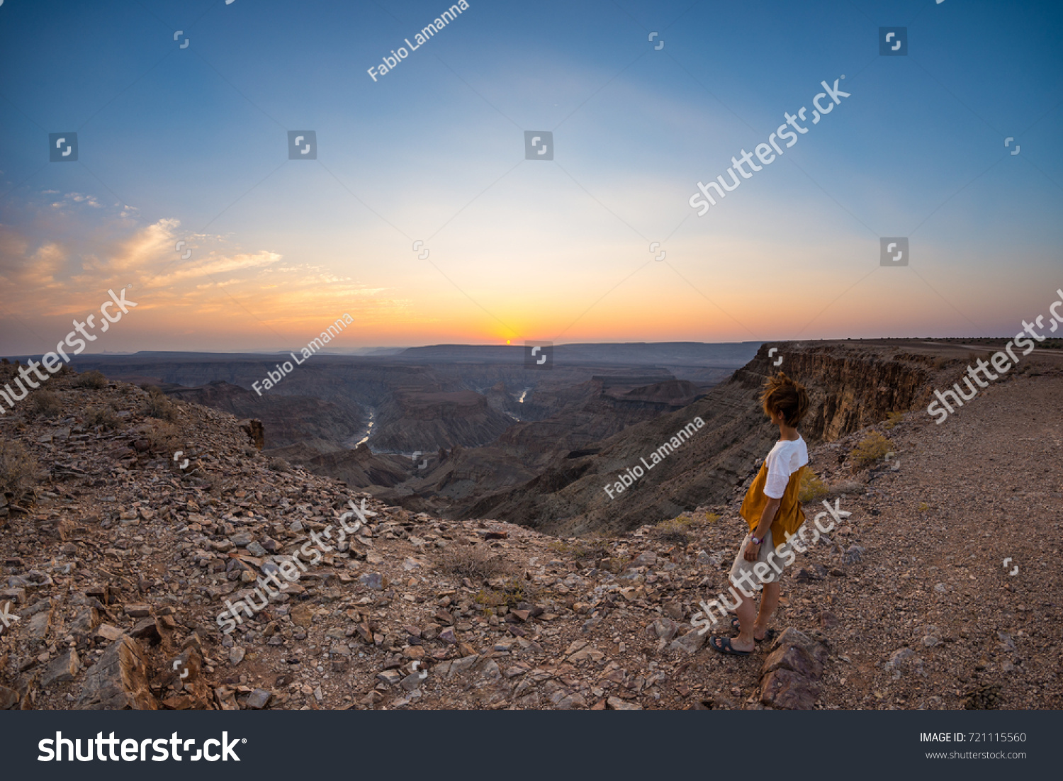 Tourist looking at the Fish River Canyon, scenic travel destination in Southern Namibia. Ultra wide angle view from above, colorful scenic sunset. #721115560