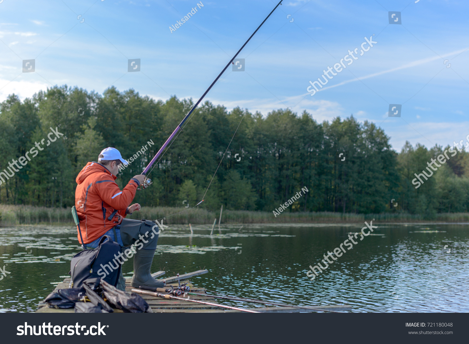 The young man catching fish on the lake from an aged pier. #721180048