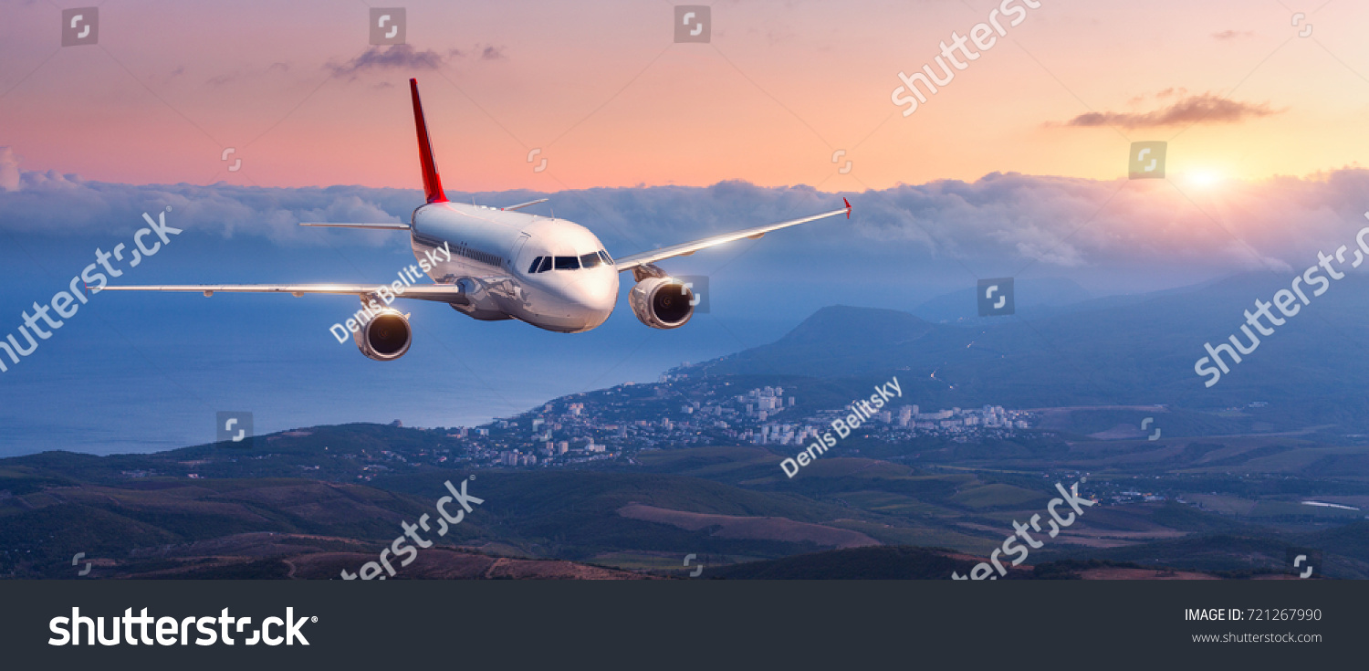 Passenger airplane. Landscape with white airplane is flying in the orange sky with clouds over mountains, sea at colorful sunset. Passenger aircraft is landing. Commercial plane. Private jet. Travel #721267990