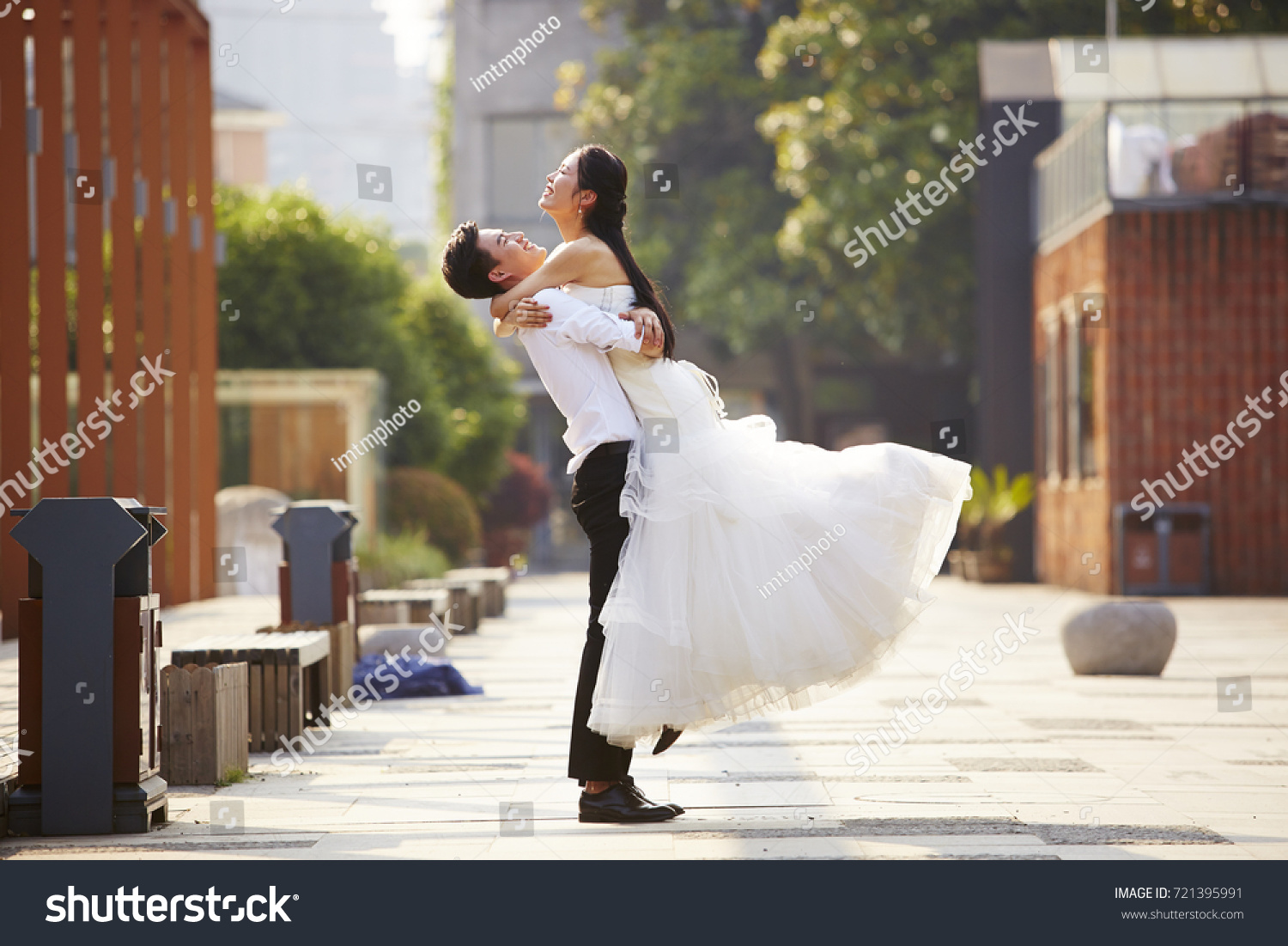 asian newly wed bride and groom celebrating marriage and hugging outside a building. #721395991
