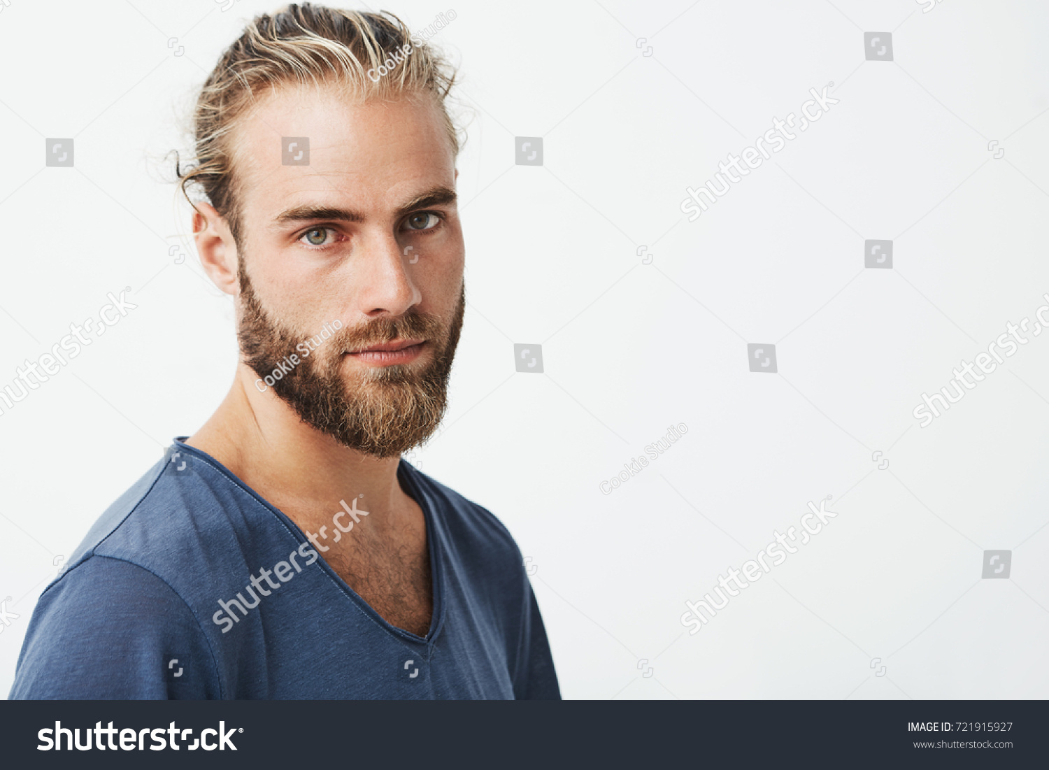Close up of beautiful swedish man with stylish hairstyle and beard in blue t-shirt looking in camera with serious expression. #721915927