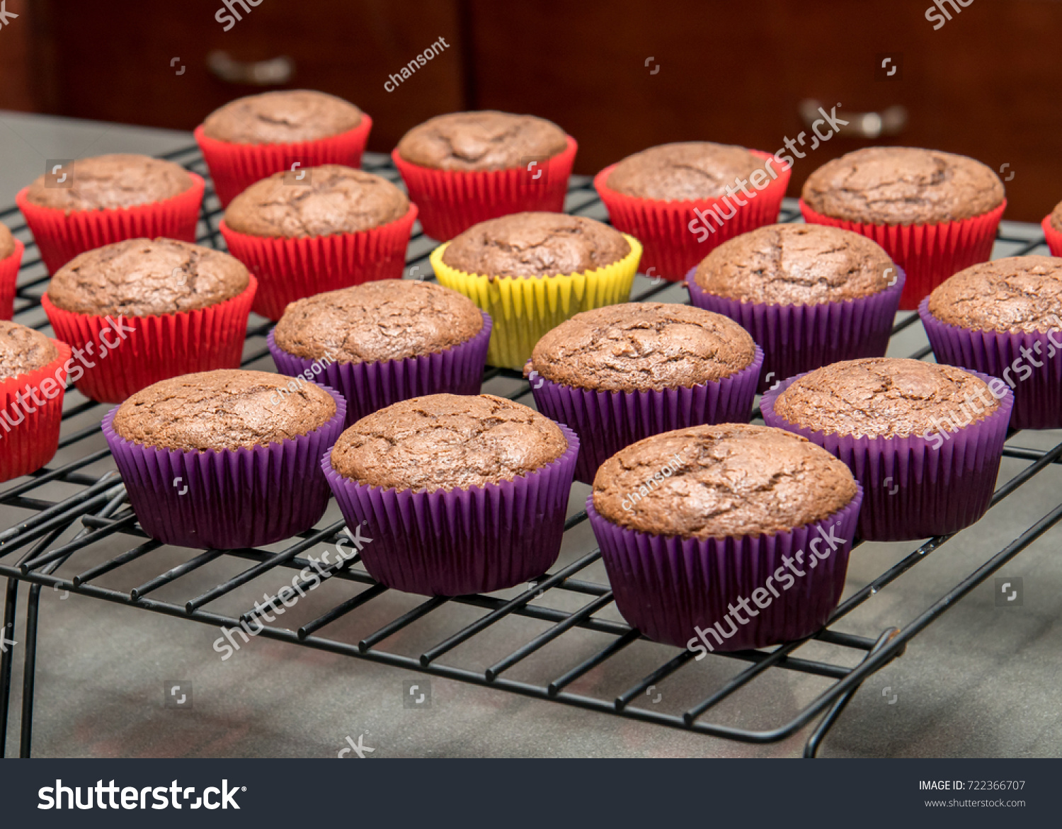 A group of cupcakes in vibrant paper wrappers cooling on a wire  #722366707