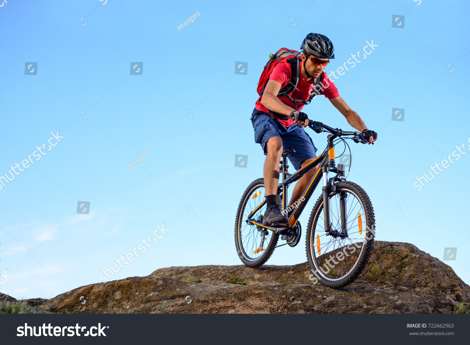 Cyclist in Red T-Shirt Riding the Bike Down the Rock on the Blue Sky Background.  #722662963
