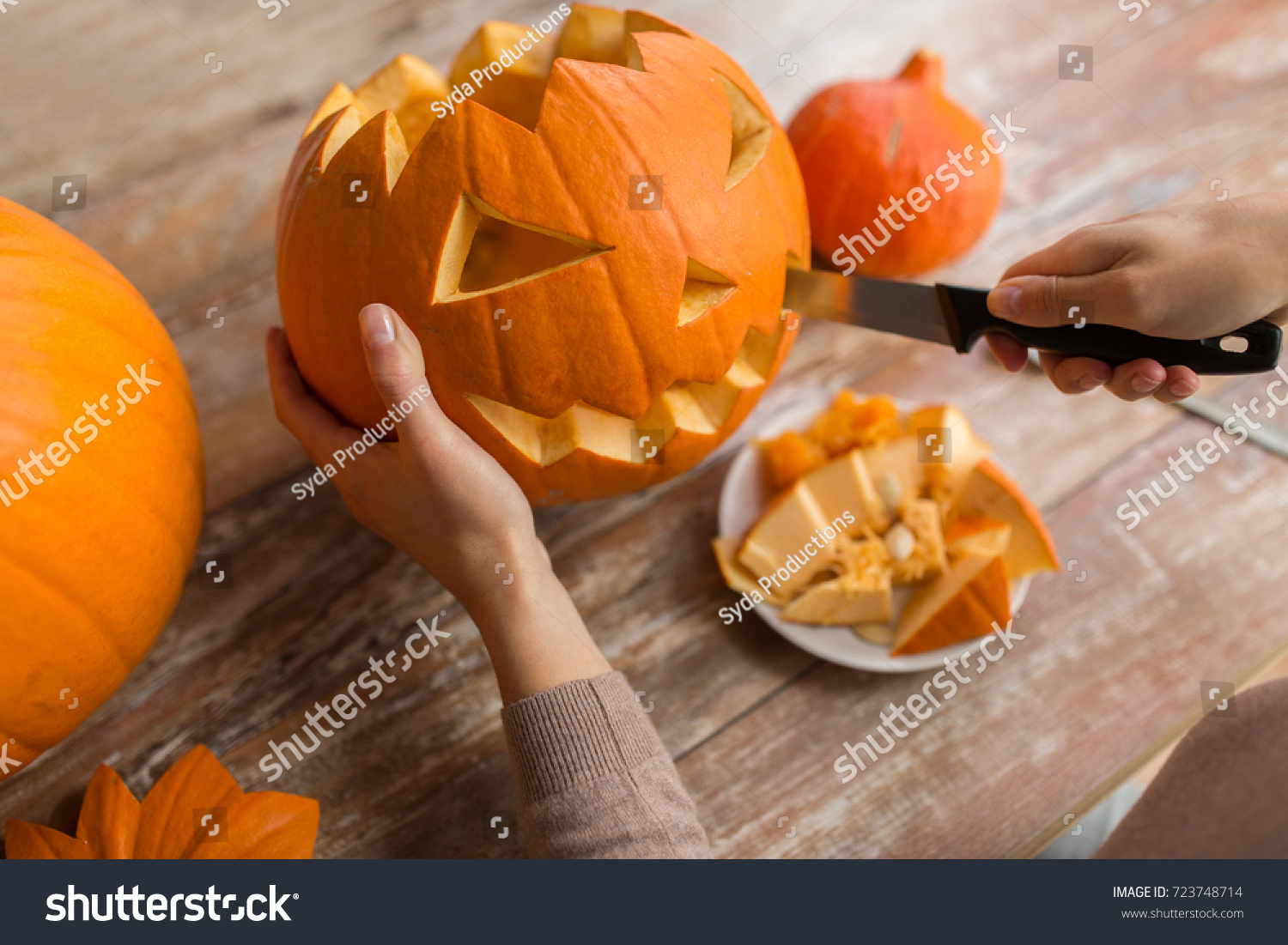 halloween, decoration and holidays concept - close up of woman with knife carving pumpkin or jack-o-lantern at home #723748714