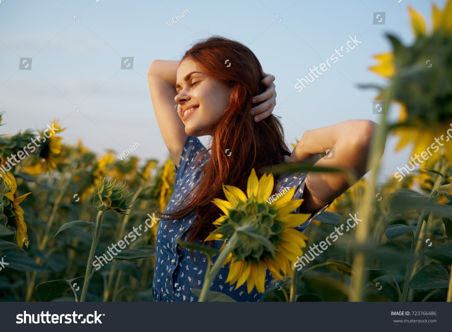 happy woman with closed eyes adjusts her hair in a field of sunflowers, a flowering of yellow flowers, nature                                #723766486