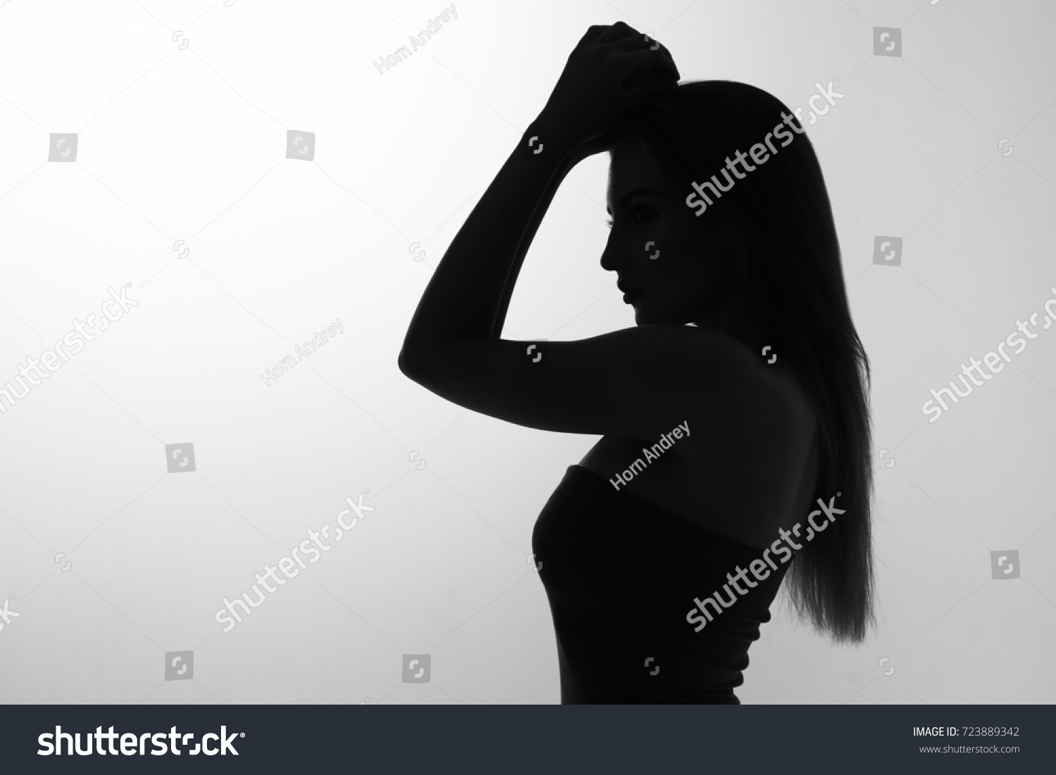 Silhouette of a beautiful sexy young woman with her hands up in her face with flowing hair on a white background #723889342