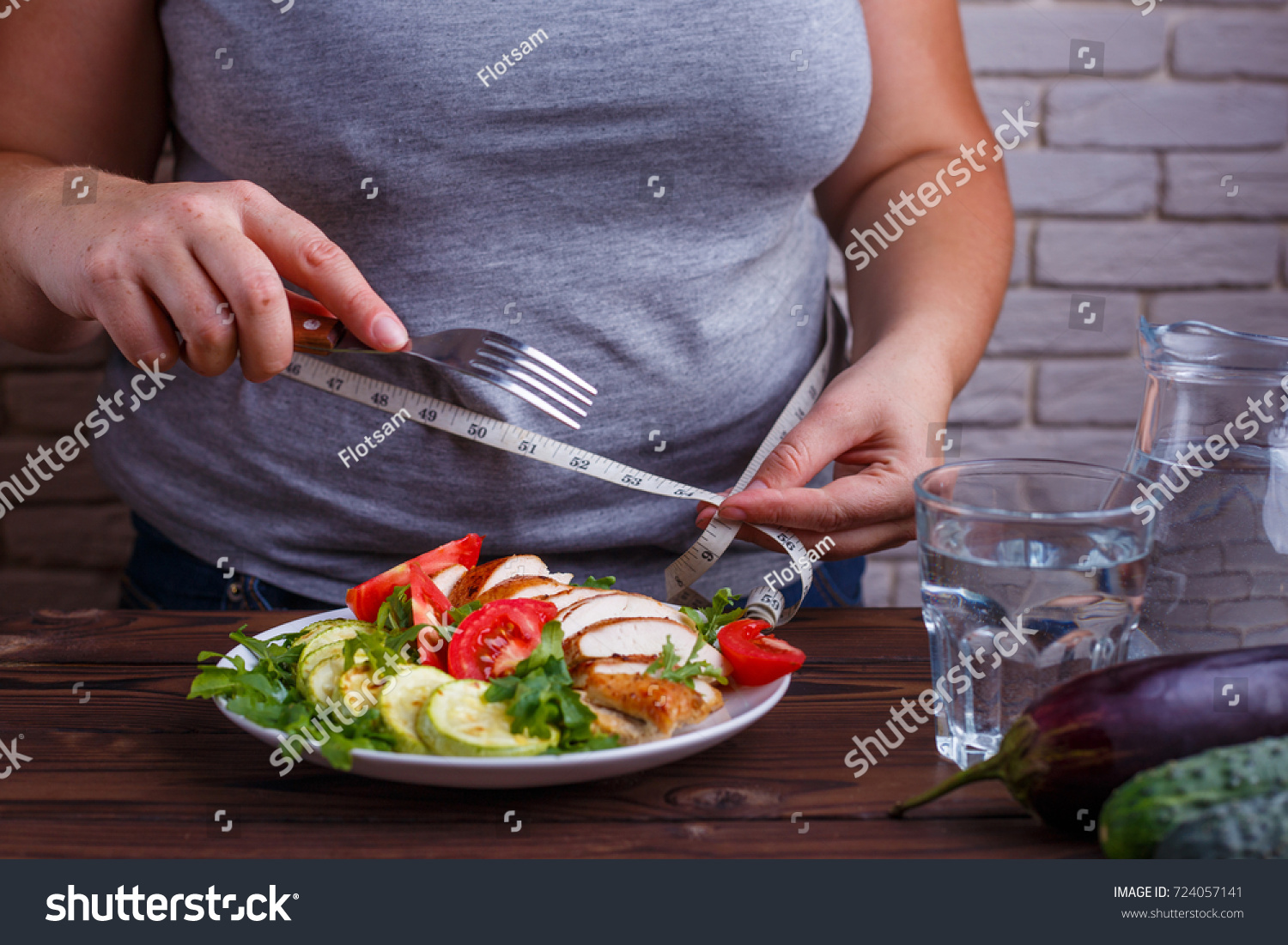 Dieting, healthy low calorie food, weight losing concept. Overweight woman with measuring tape on her waist eating salad from a bowl #724057141