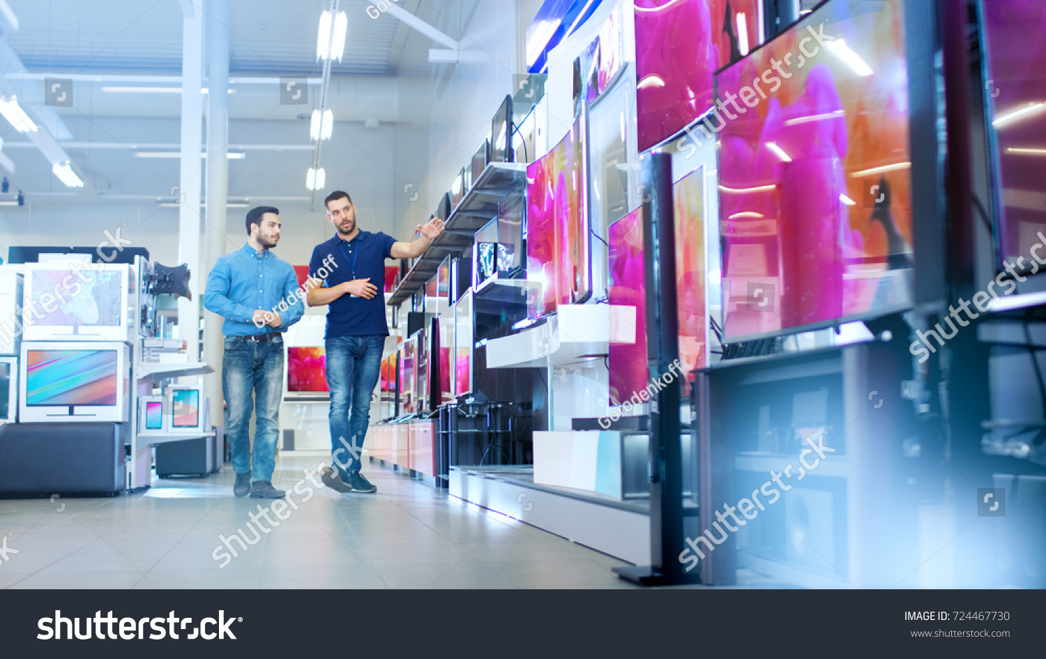 In the Electronics Store Professional Consultant Shows Latest 4K UHD TV's to a Young Man, They Talk about Specifications and What Model is Best for Young Man's Home. Store is Bright. #724467730