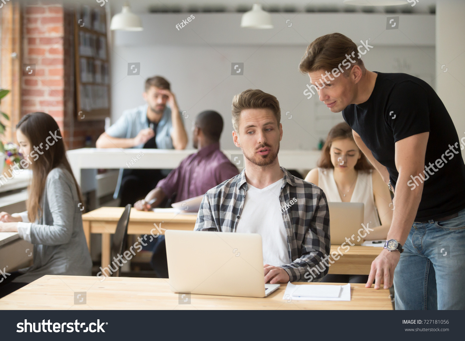 Casual entrepreneur explaining business project to his coworker. Two young employees discuss work-related goals in front of laptop at workplace in shared office. Team discussing marketing strategies.  #727181056