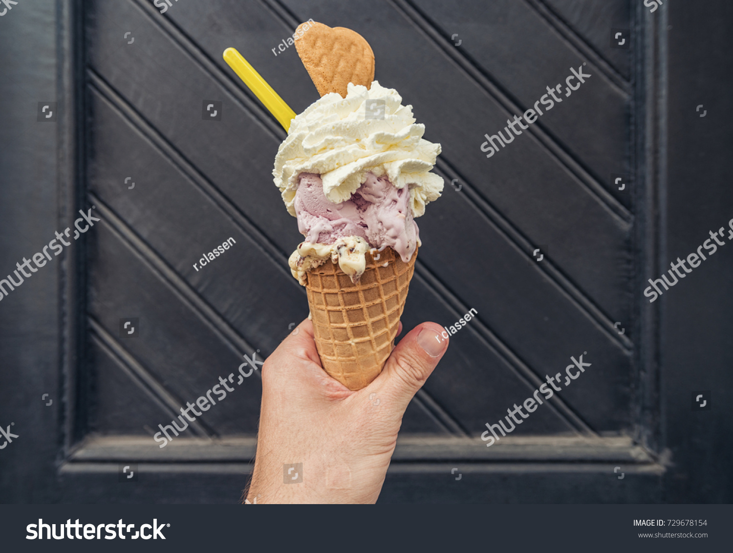 Male hand holding ice cream with cream and cookie against black  #729678154
