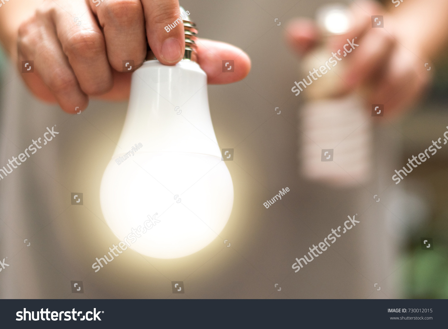 Power saving concept. Hands holding  new  Light Emitting Diode ( LED ) light bulb with light on and blur spiral compact-fluorescent (CFL) bulbs behind for copyspace. #730012015