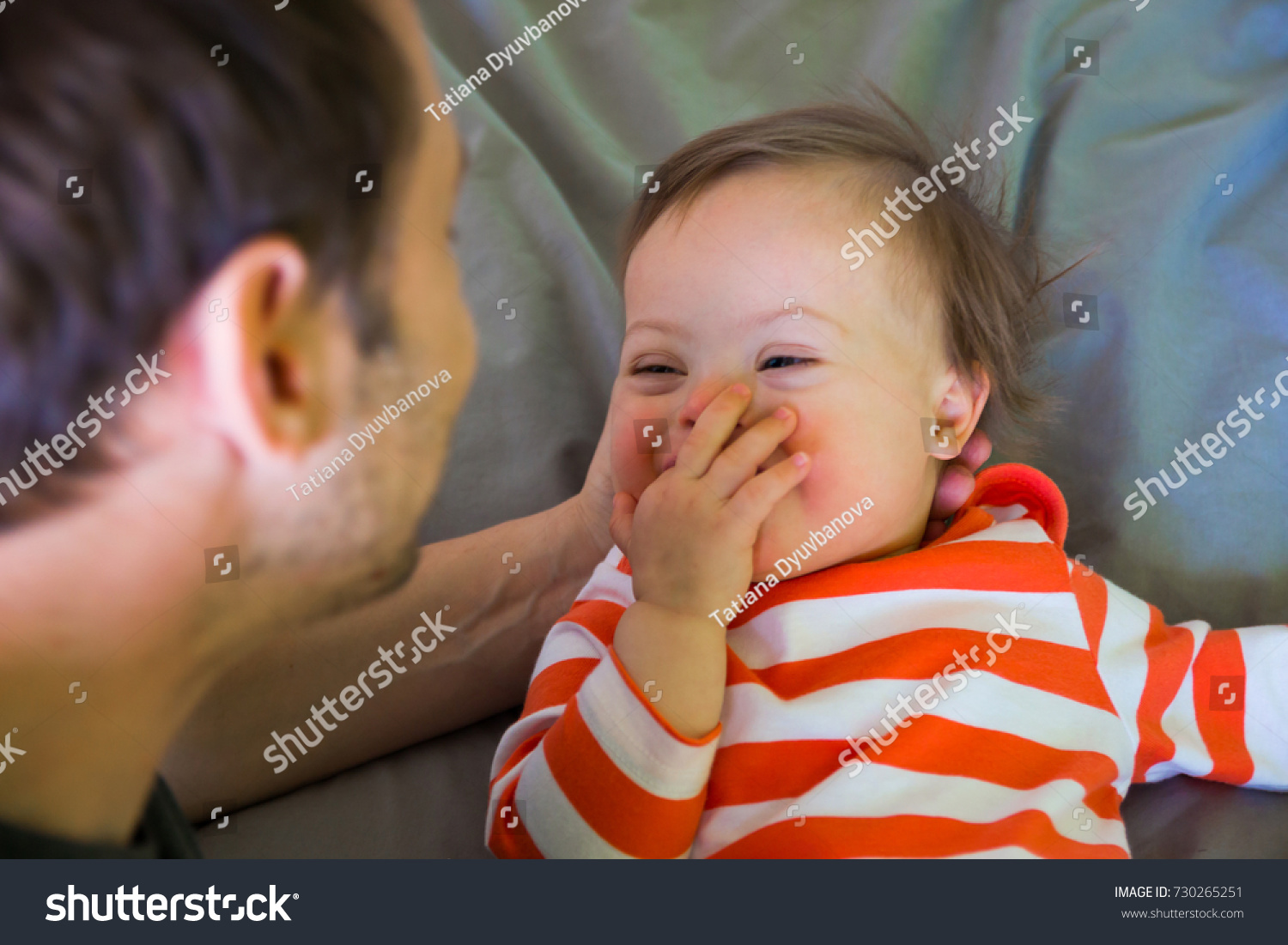Cute baby boy with Down syndrome playing with dad on the bed in home bedroom #730265251
