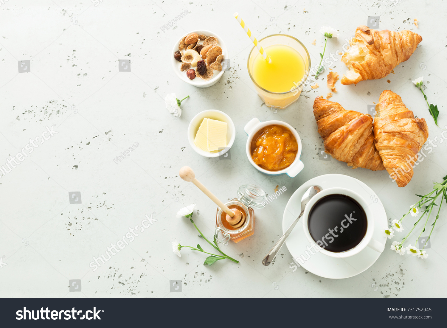 Continental breakfast captured from above (top view, flat lay). Coffee, orange juice, croissants, jam, honey and flowers. Grey stone worktop as background. Layout with free text (copy) space. #731752945