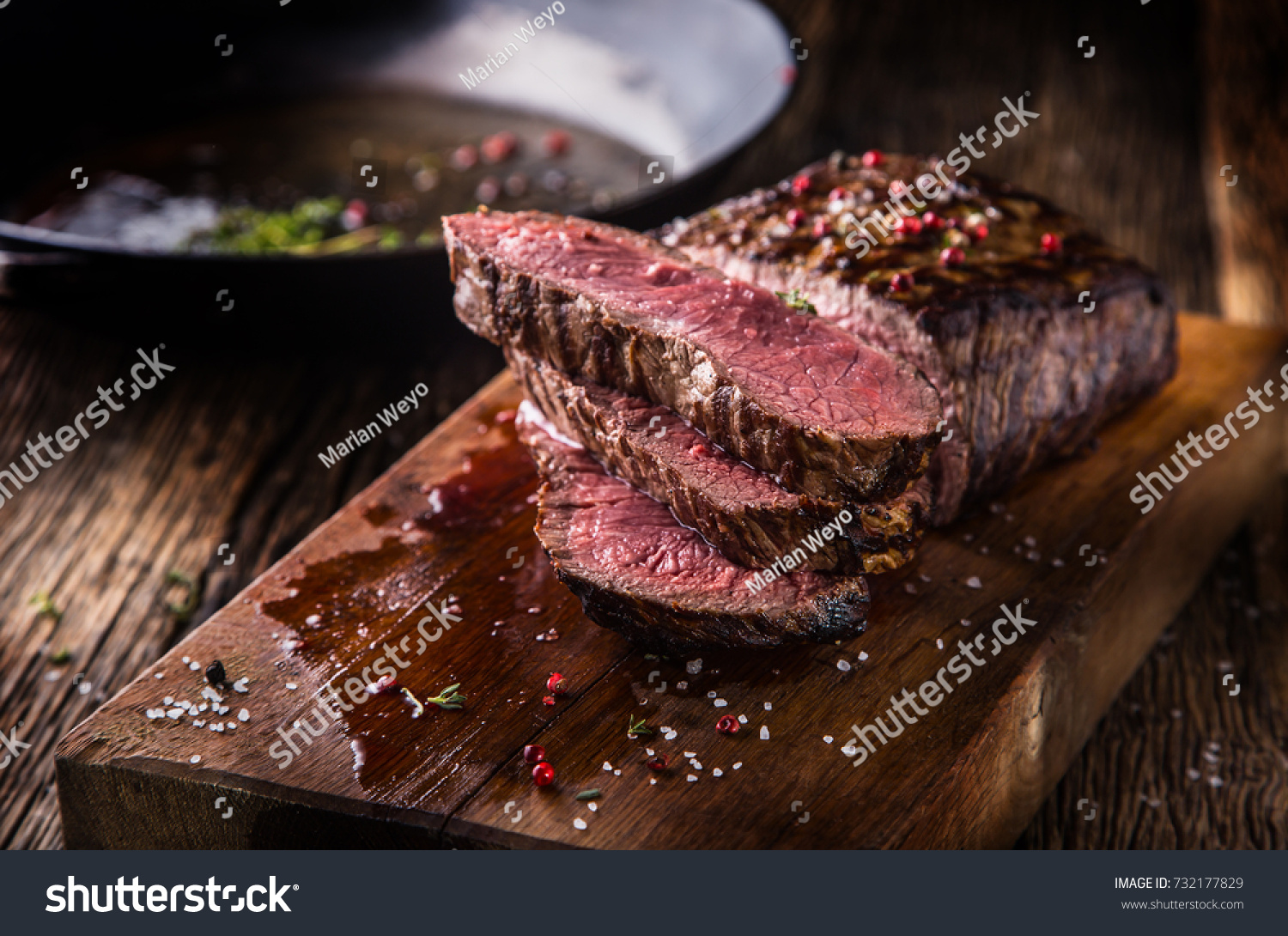 Juicy medium Beef Rib Eye steak slices in pan on wooden board with fork and knife herbs spices and salt. #732177829