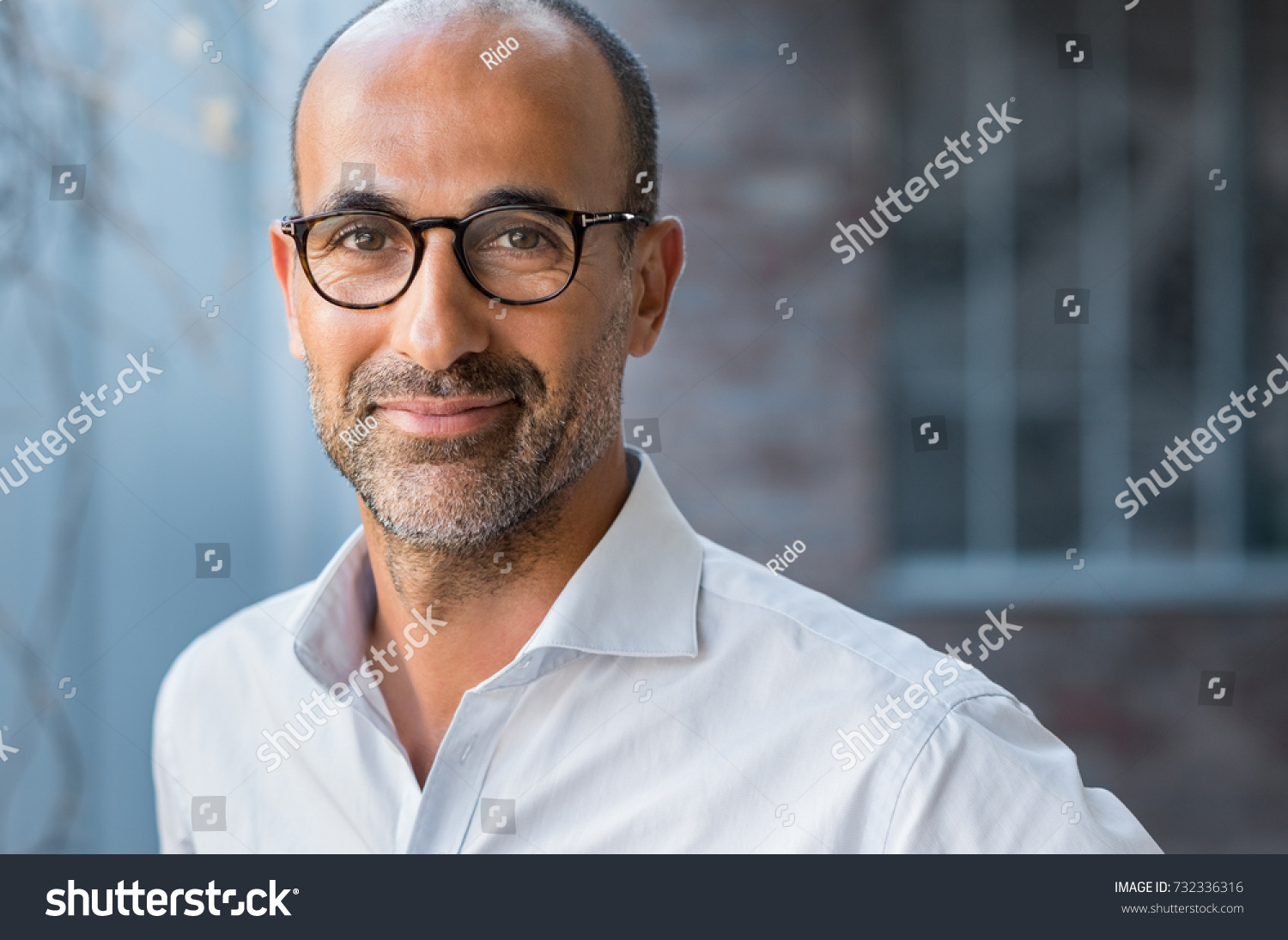 Portrait of happy mature man wearing spectacles and looking at camera outdoor. Man with beard and glasses feeling confident. Close up face of hispanic business man smiling.