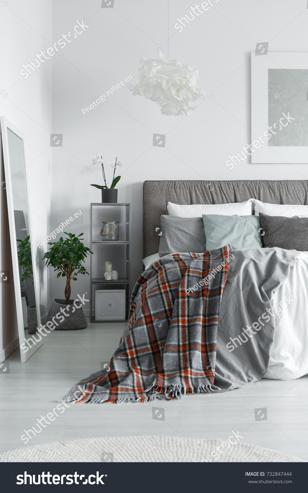 Cozy interior of a monochromatic bedroom with a king-size bed and checkered bedclothes lying on it #732847444
