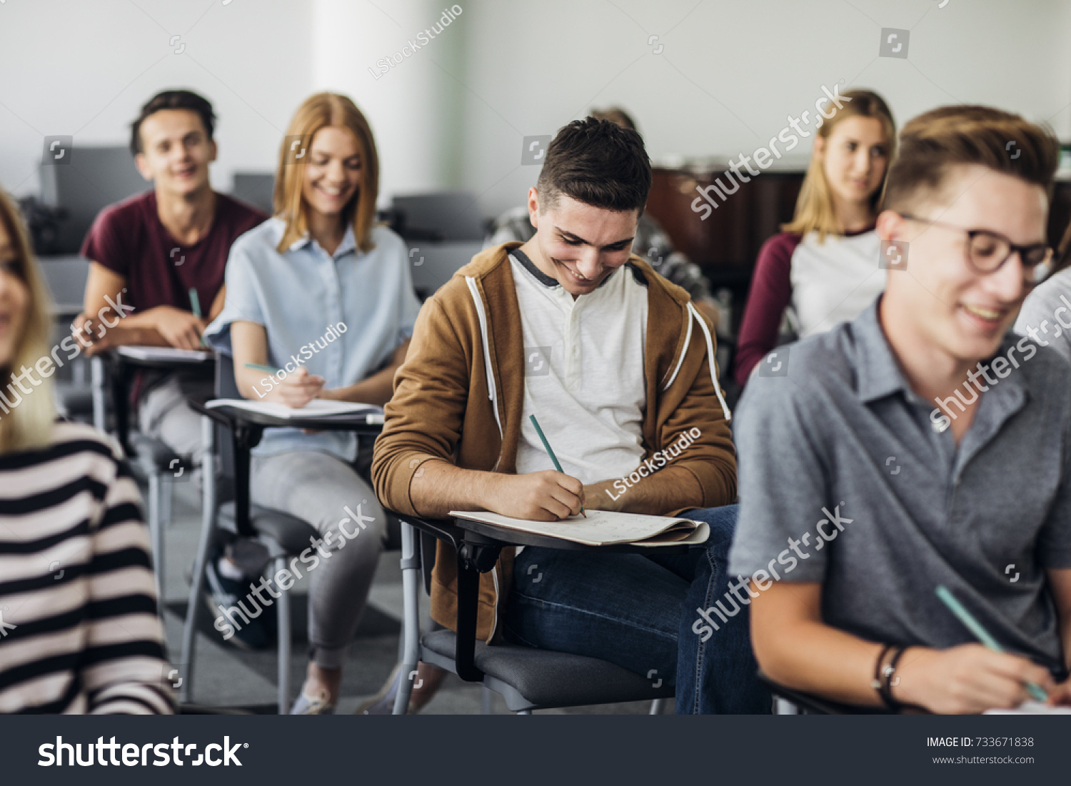 Group of high school students sitting in classroom and writing in notebooks. #733671838