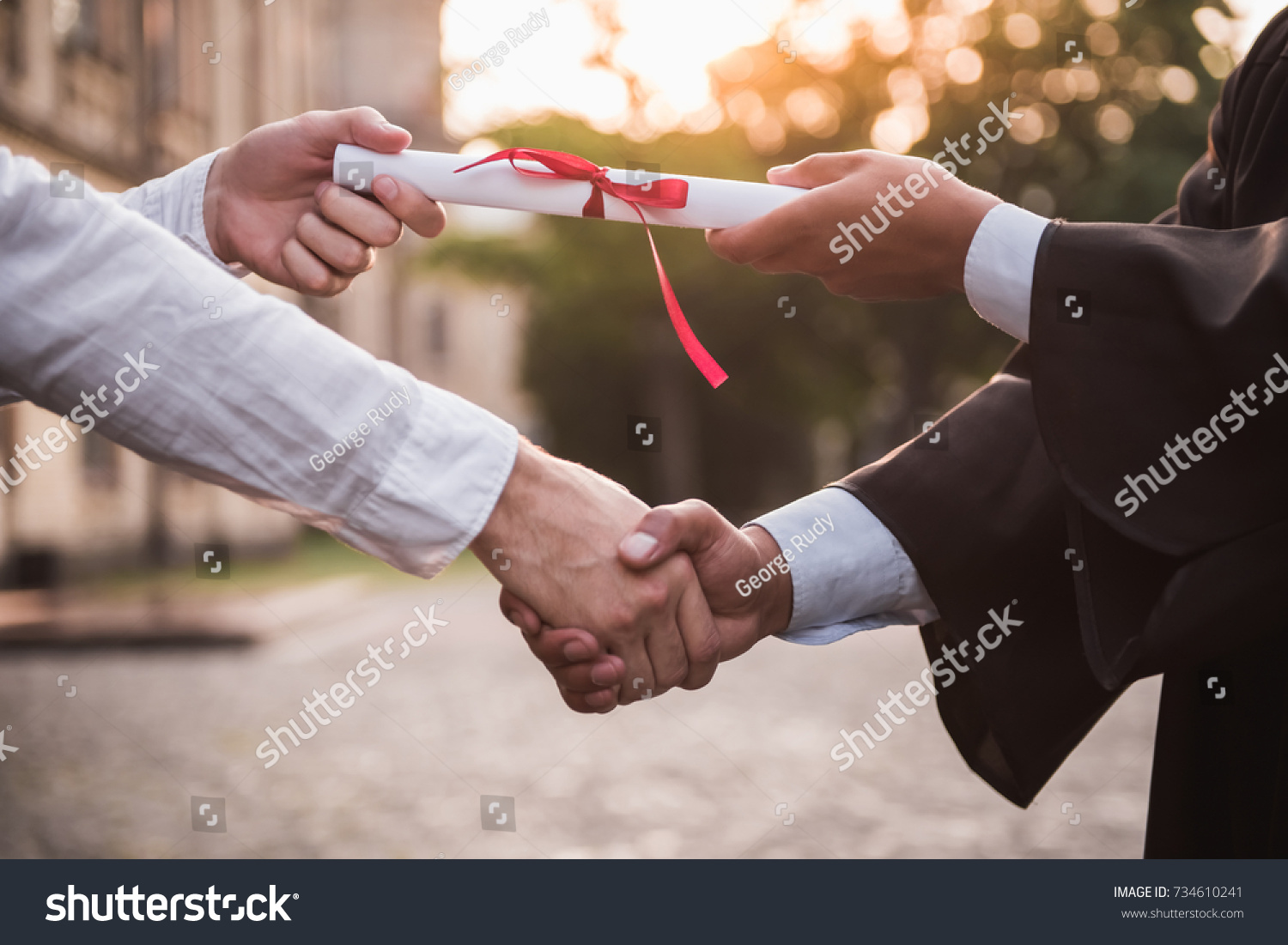 Cropped image of graduate in academic dress taking his diplomas and shaking hand #734610241