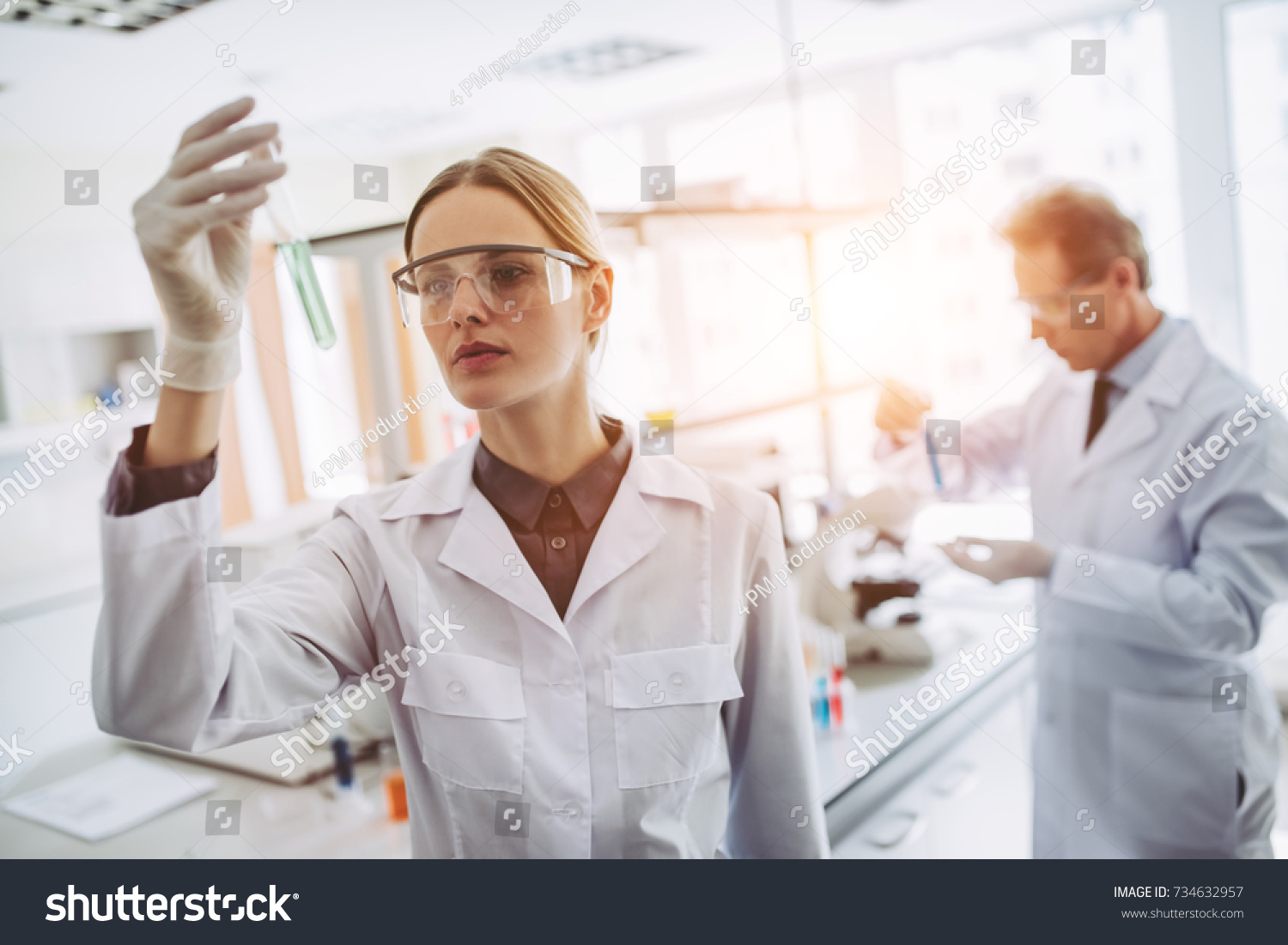 Two scientists are working in laboratory. Young female researcher and her senior supervisor are doing investigations with test tubes. #734632957