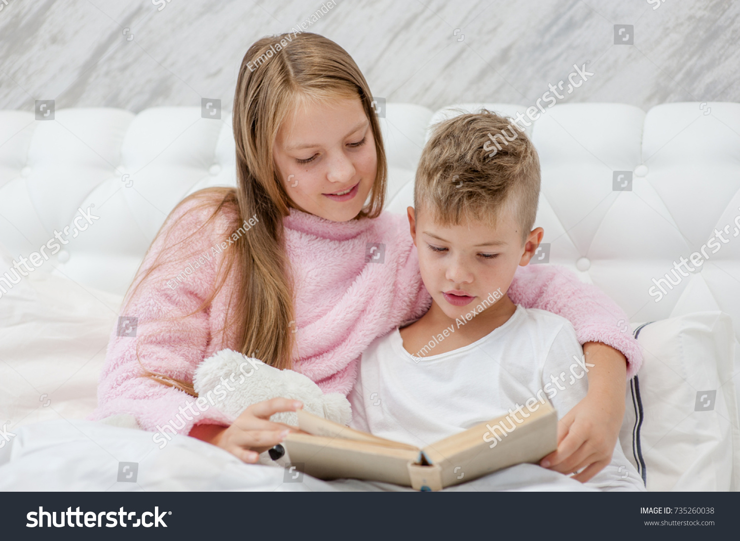 brother and sister read a book on the bed. #735260038