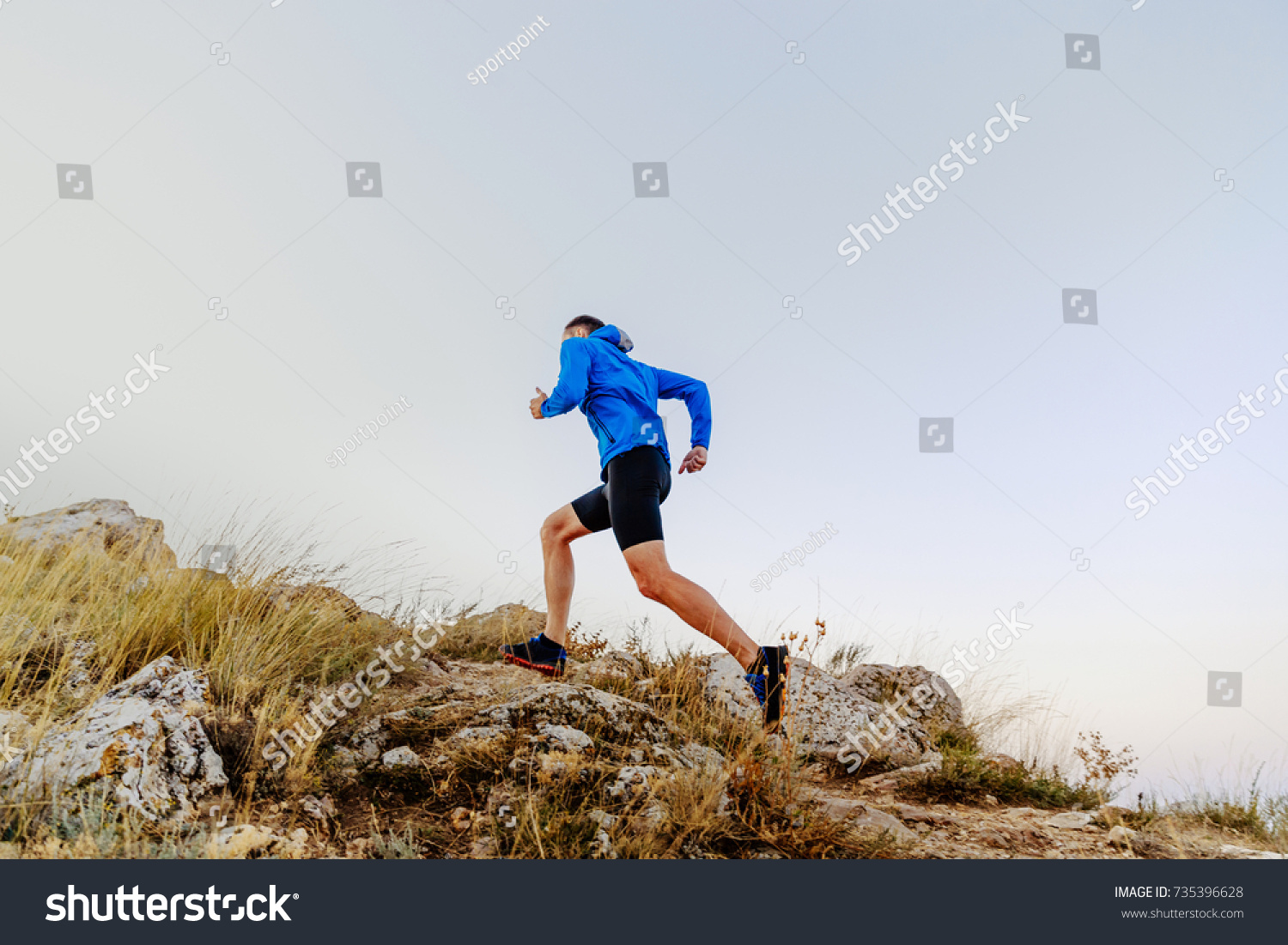 running uphill on stones male athlete runner side view #735396628