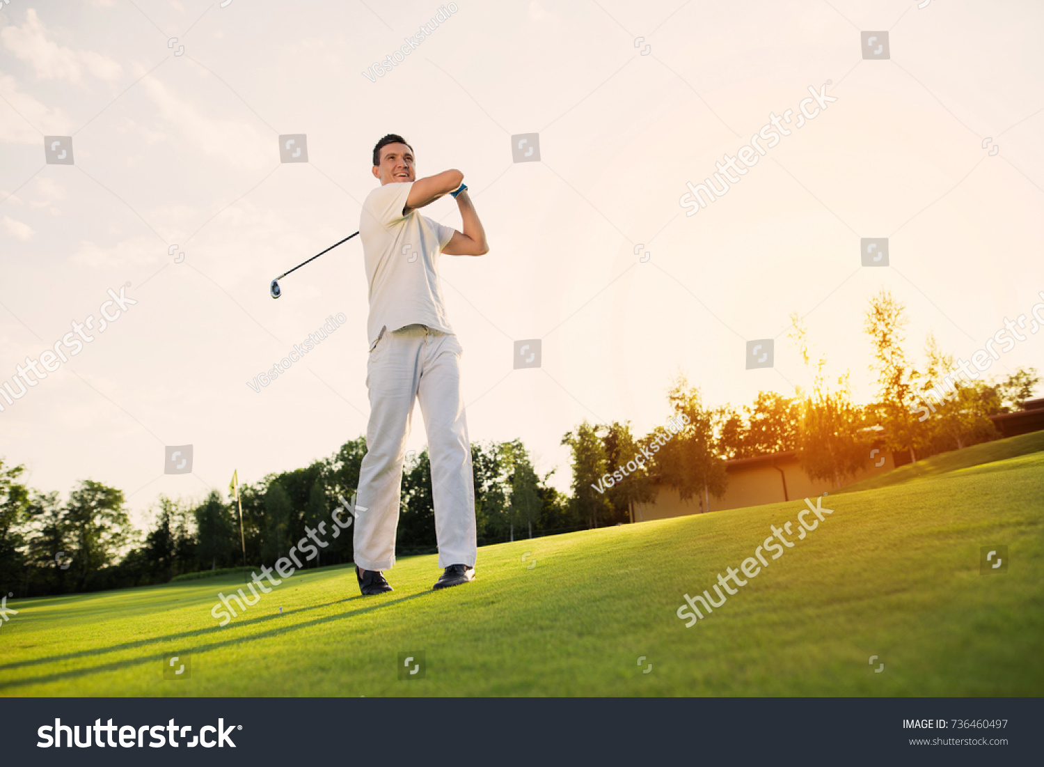 A man in a white suit is playing golf and just hit. He smiles, because the blow was excellent #736460497