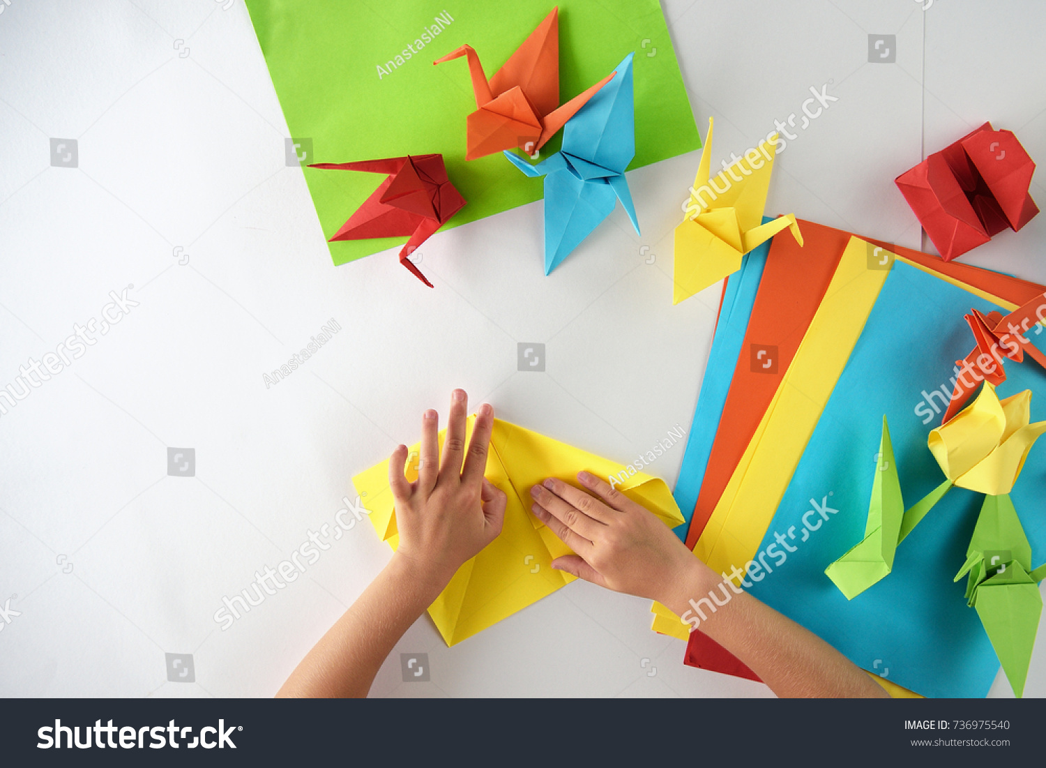 Children's hands do origami from colored paper on white background. lesson of origami #736975540