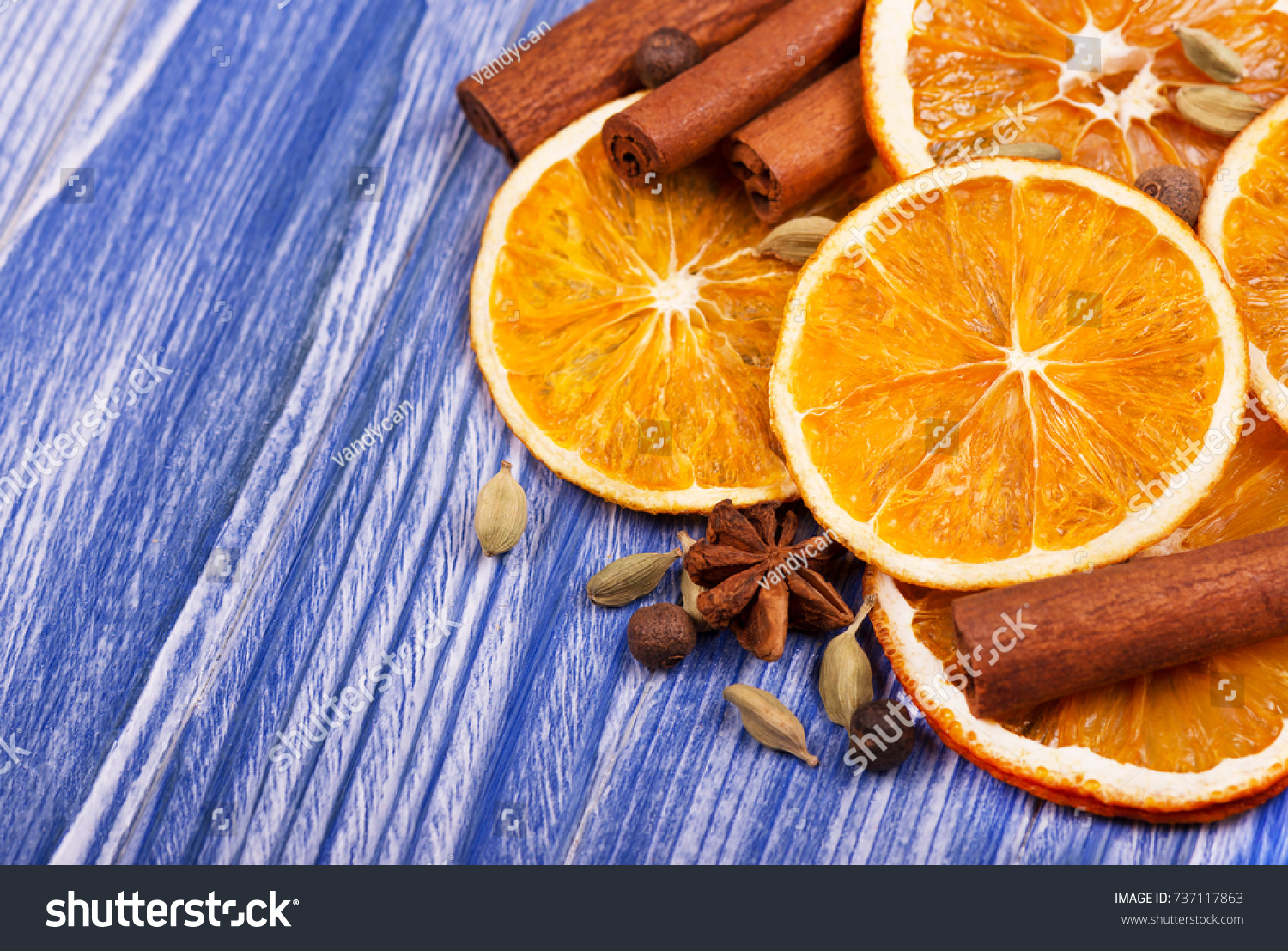 Dry slices of orange, cinnamon, allspice and cardamom on a blue wooden background #737117863