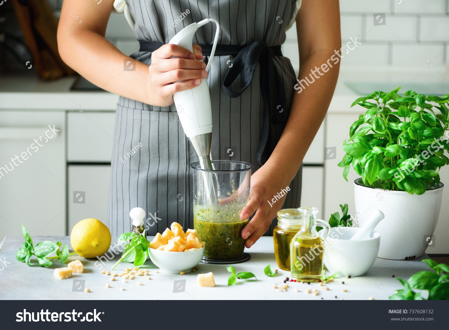 Woman using hand blender to make pesto. White kitchen interior design. Copy space. Vegetarian, clean eating lifestyle concept #737608132