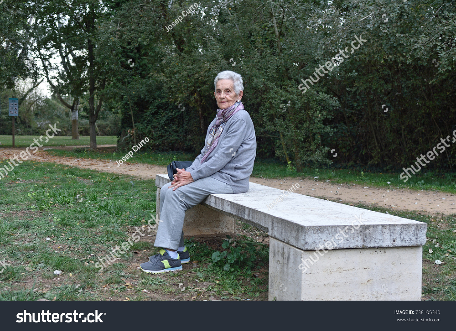 senior woman sitting alone on a bench in a park #738105340