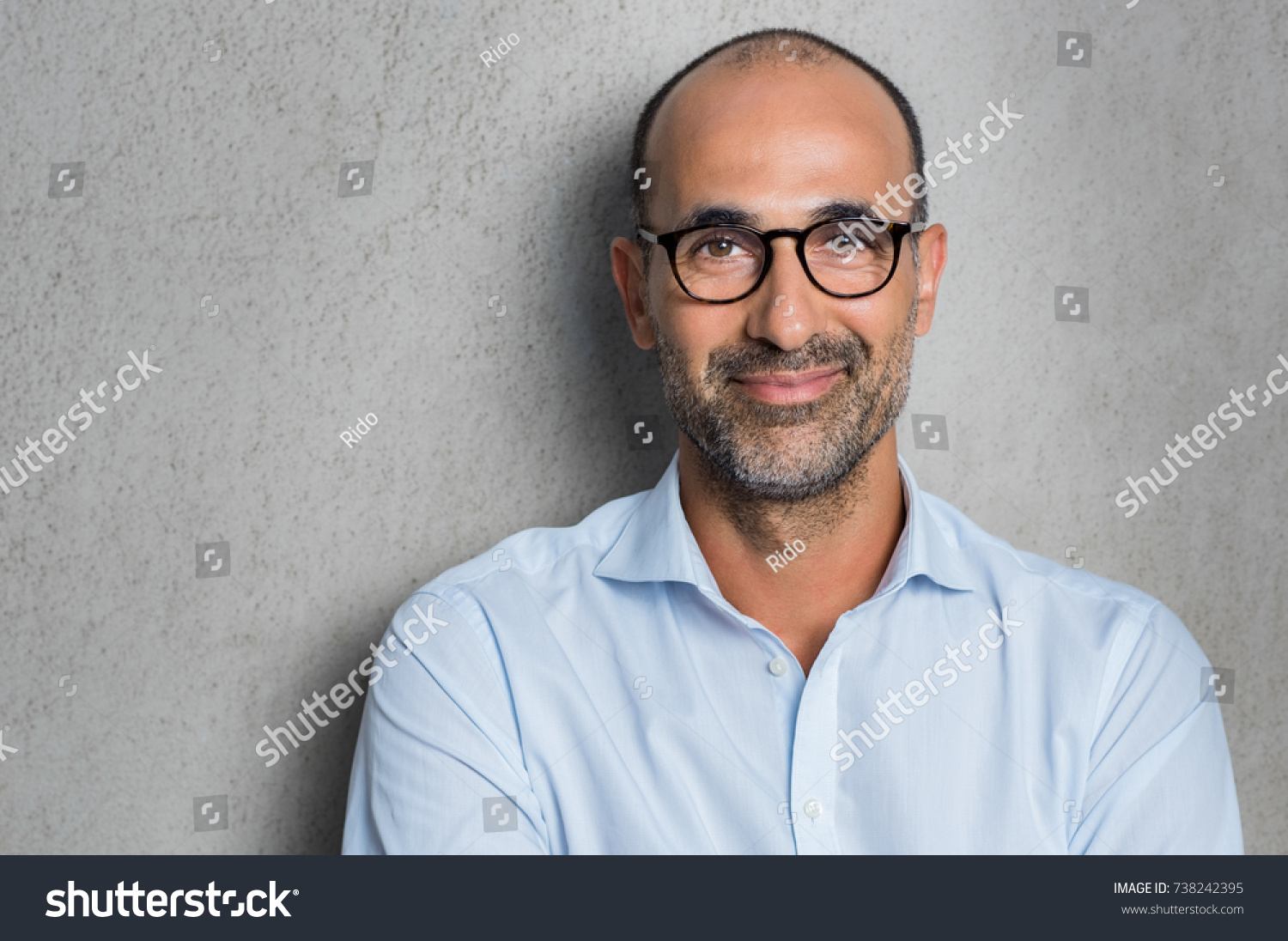 Portrait of a mature businessman wearing glasses on grey background. Happy senior latin man looking at camera isolated over grey wall with copy space. Close up face of happy successful business man.