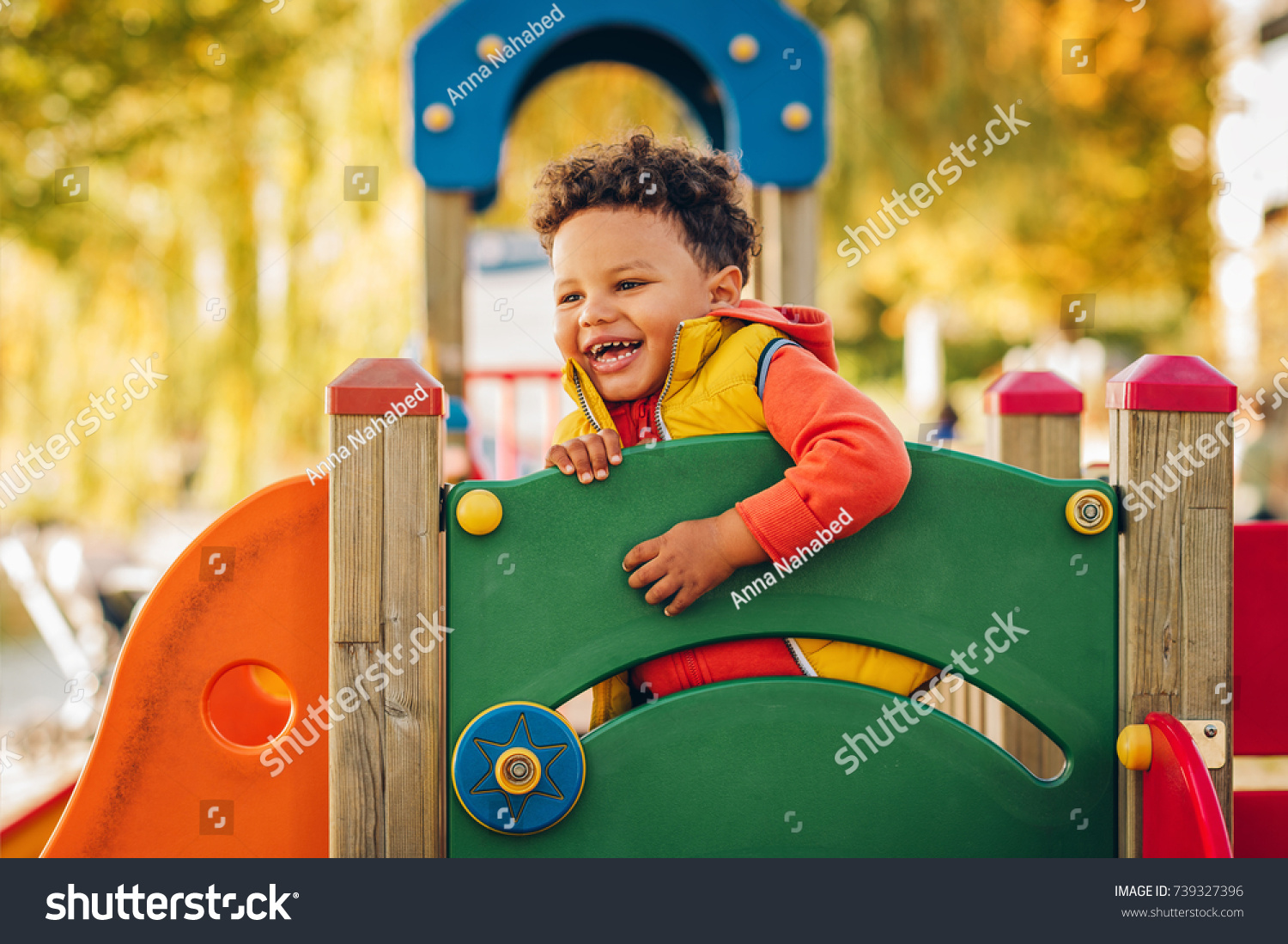 Adorable little 1-2 year old toddler boy having fun on playground, child wearing orange hoody jacket and yellow vest  #739327396