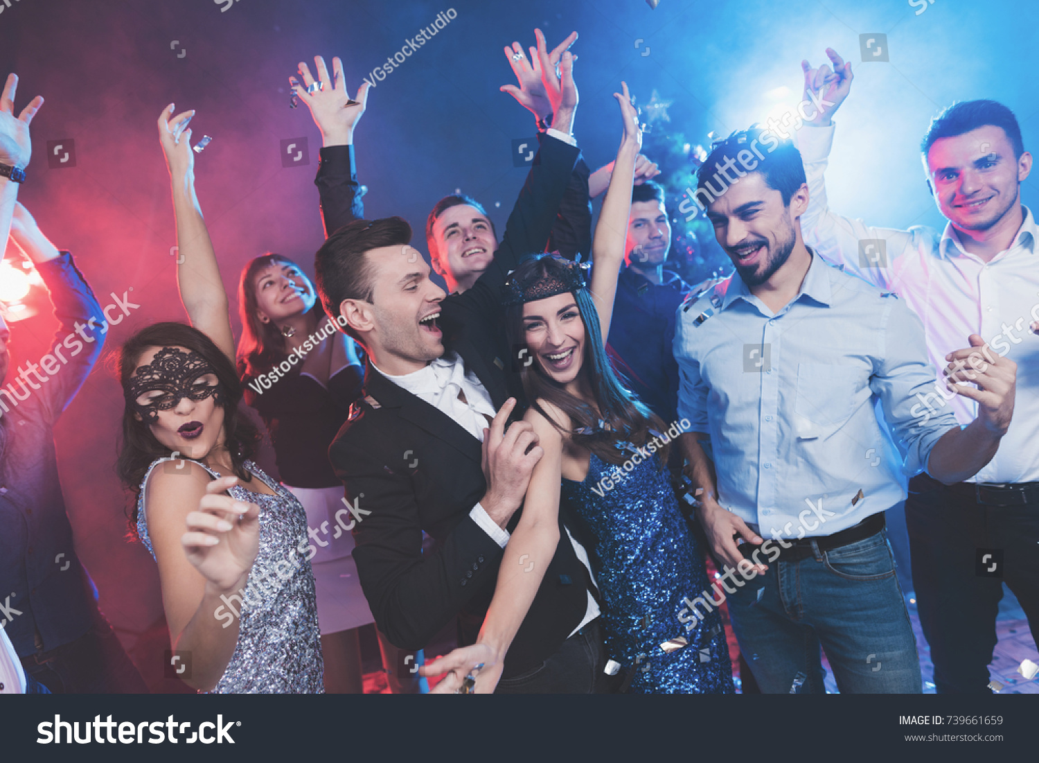 New Year party. Young couple dancing with glasses of champagne in hands. Against the background, young people's friends are dancing. Around fly confetti and there is white smoke. #739661659