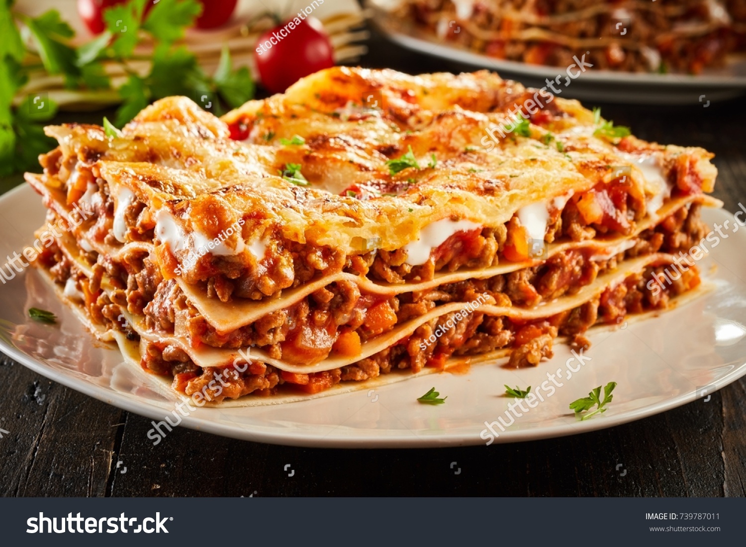 Portion of succulent ground beef lasagne topped with melted cheese and garnished with fresh parsley served on a plate in a close up view for a menu #739787011