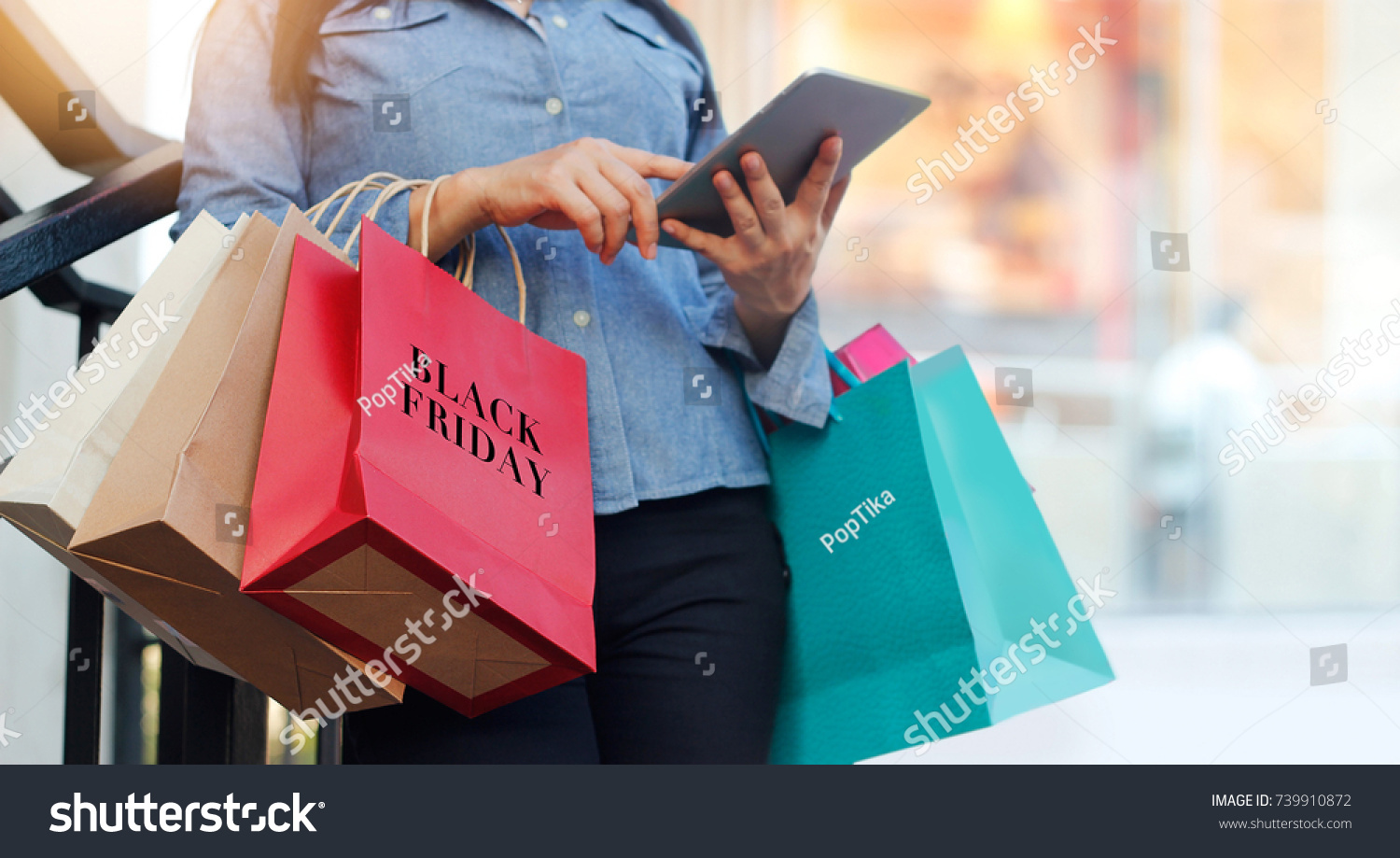 Woman using tablet and holding Black Friday shopping bag while standing on the stairs with the mall background #739910872
