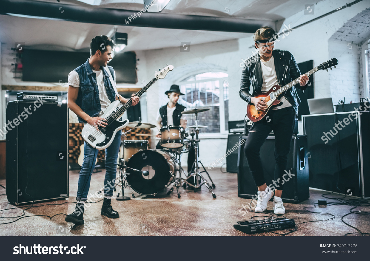 Repetition of rock music band. Bass guitar player, electric guitar player and drummer behind the drum set. Rehearsal base #740713276