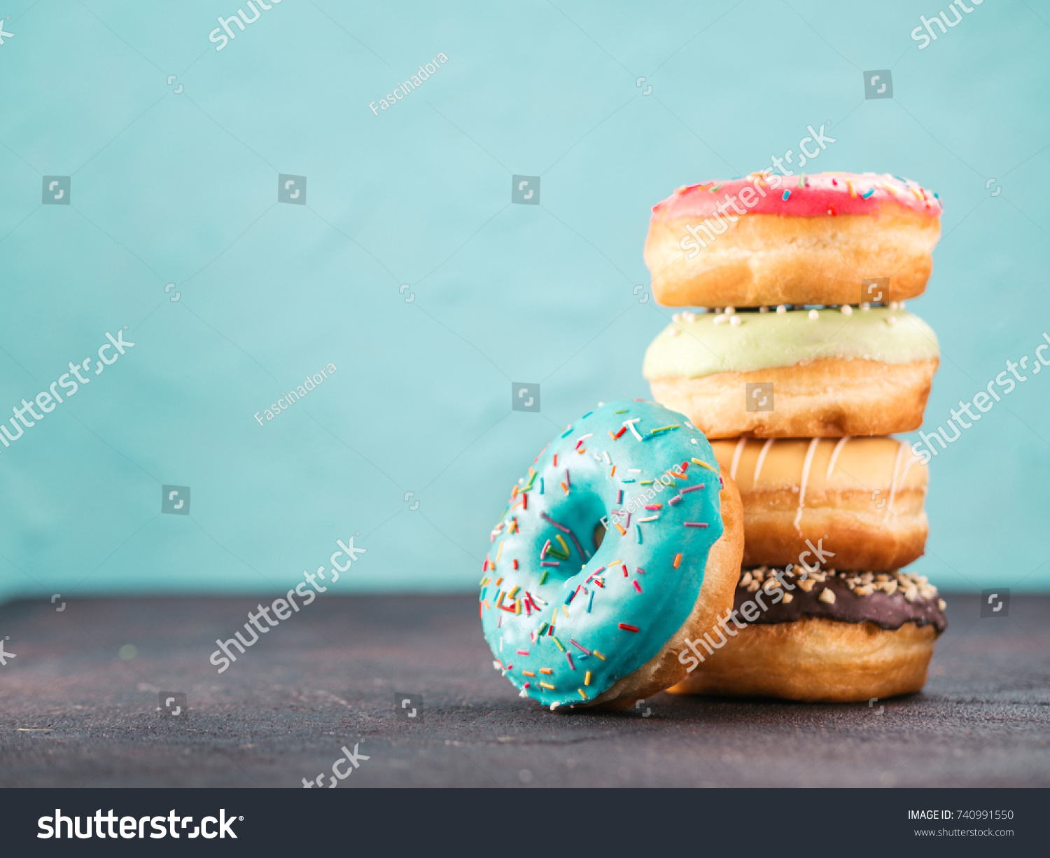 Stack of assorted donuts on black and blue cement background. Blue glazed doughnut with sprinkles on foreground. Copy space. Shallow DOF #740991550