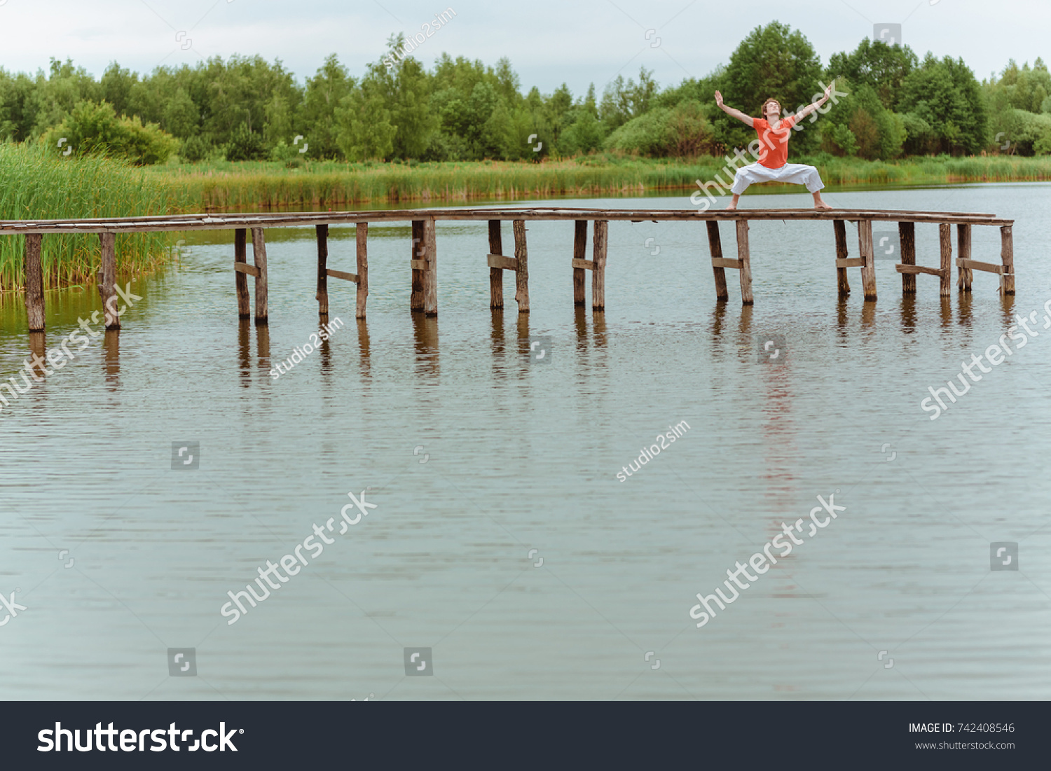 A man doing yoga on wooden pier at the lake #742408546