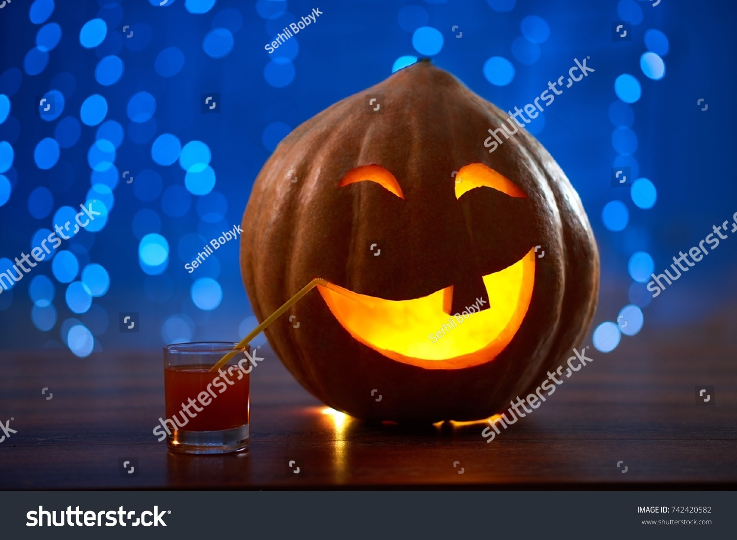 Halloween pumpkin jack face lantern with a candle burning placed on the table with a cocktail copyspace party festive celebrating mood fun autumn concept. #742420582