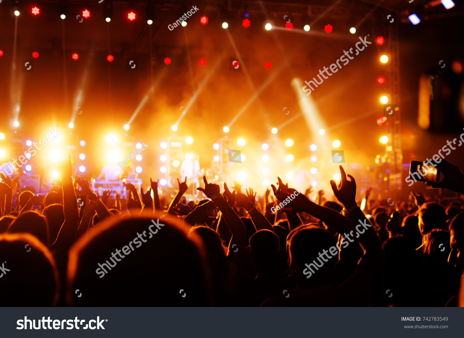silhouettes of concert crowd and mohawk punk hair style in front of bright stage lights #742783549