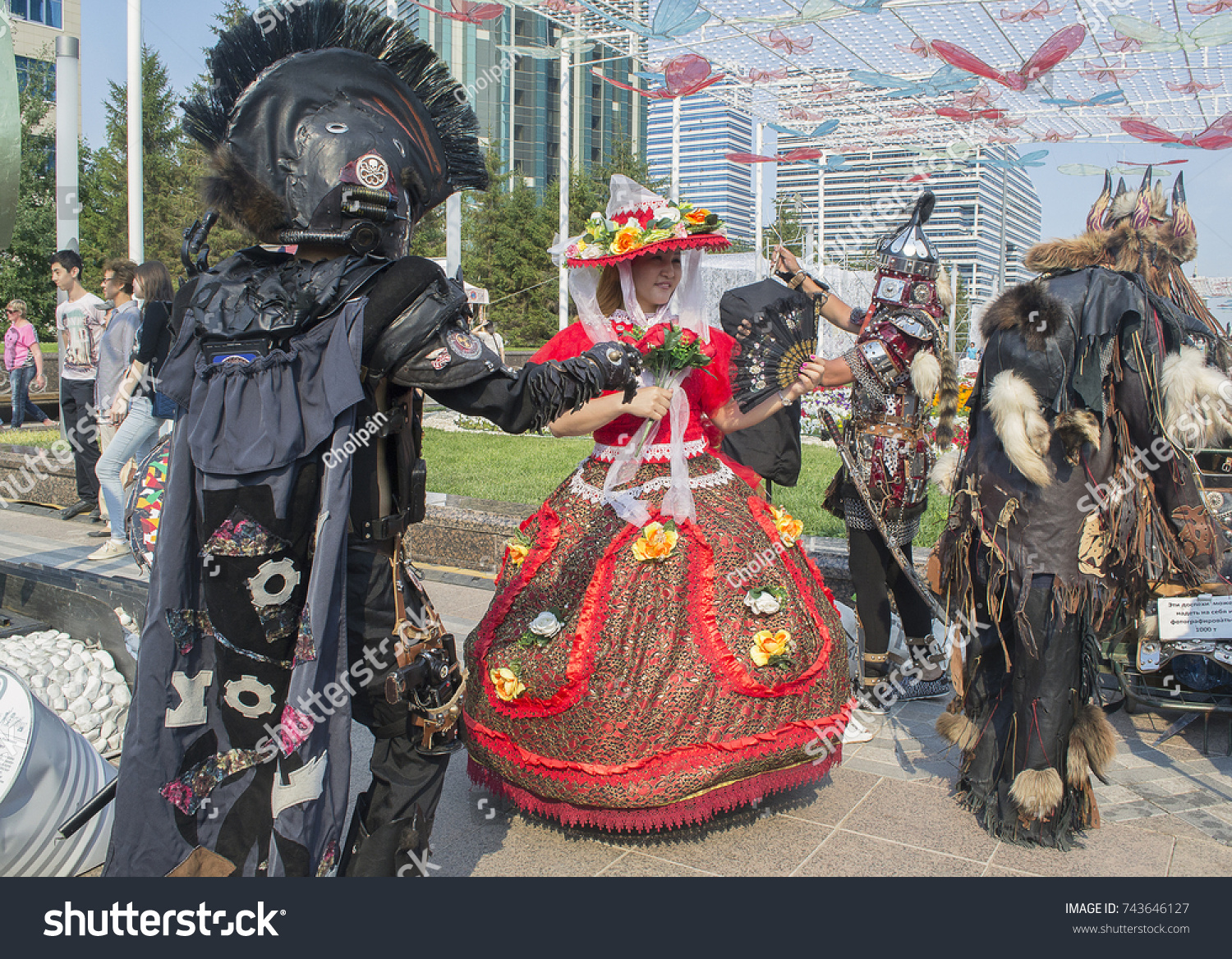 Astana, Kazakhstan - July 6, 2017: Street entertainment, costume hire. Young Kazakh woman in fancy dress of fairy & 3 men rigged out as knight, legionary & shaman #743646127