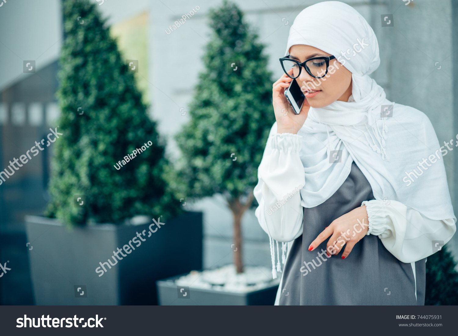 Happy young muslim woman with glasses talking on mobile phone at city street lifestyle portrait. outdoors #744075931